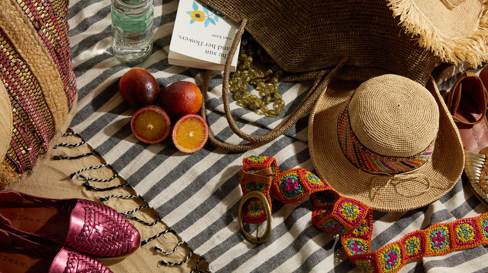 A beach blanket with hats, sunglasses, and a book.