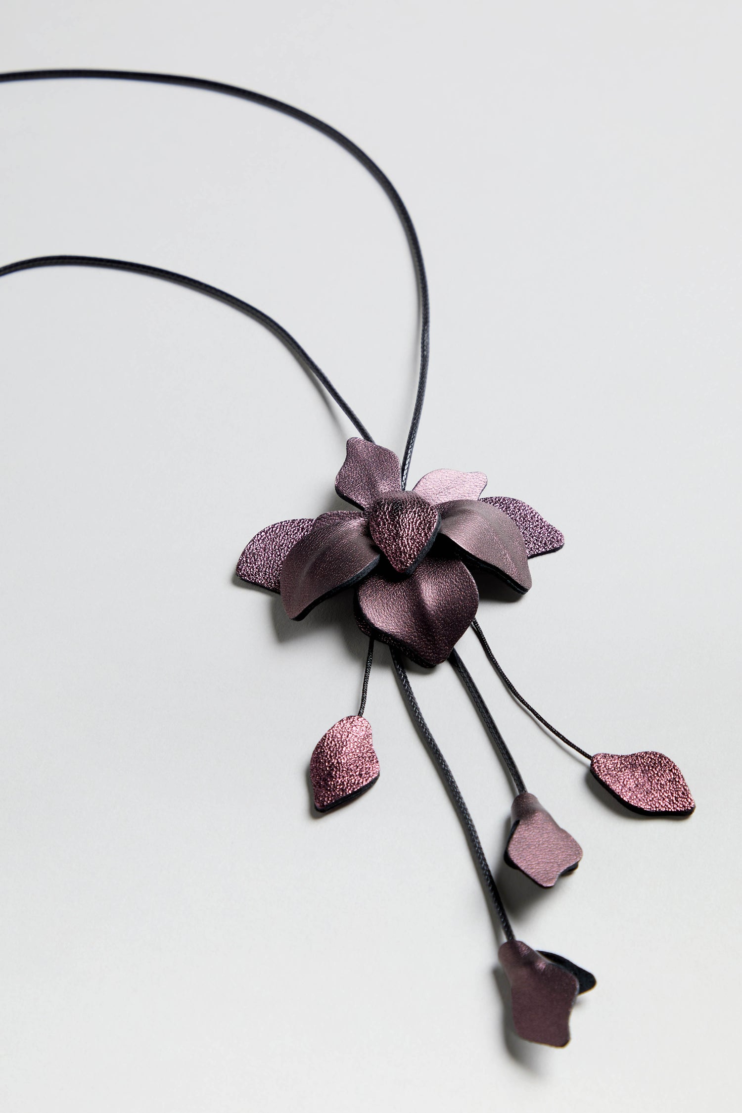 Metallic Leather Flower Necklace with dark purple petal and leaf-shaped charms on black cords, perfect as statement jewelry, shown on a light gray background.