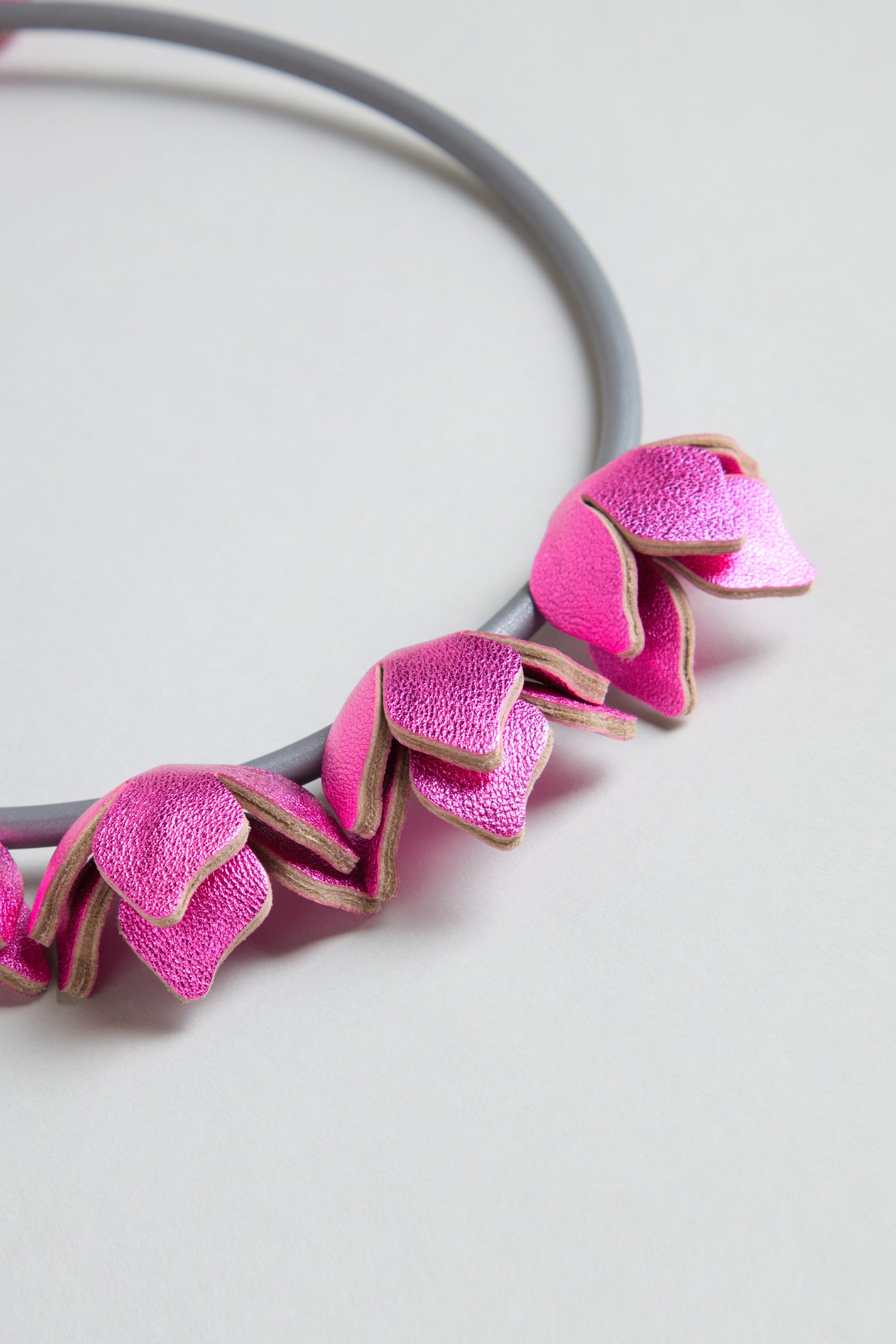 The Short Leather Petals Necklace features several metallic pink petal-shaped charms and is displayed on a light background, adding a chic touch to any look.