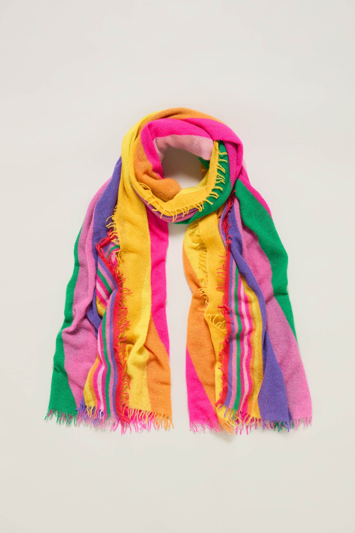 The Colour Pop Stripe Cashmere Scarf features wide, vibrant vertical stripes in pink, yellow, green, purple, and orange with frayed edges and is displayed on a light background.
