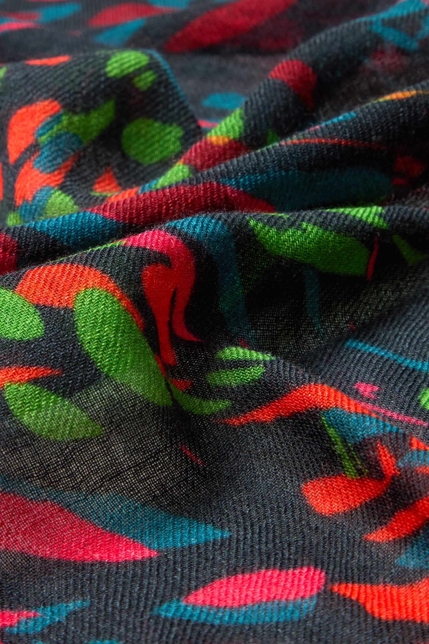 Close-up of the Skyfire Scarf—a textured black wool-silk accessory with vibrant abstract red, green, blue, and orange patterns. Elegant folds and creases highlight this true luxury piece.