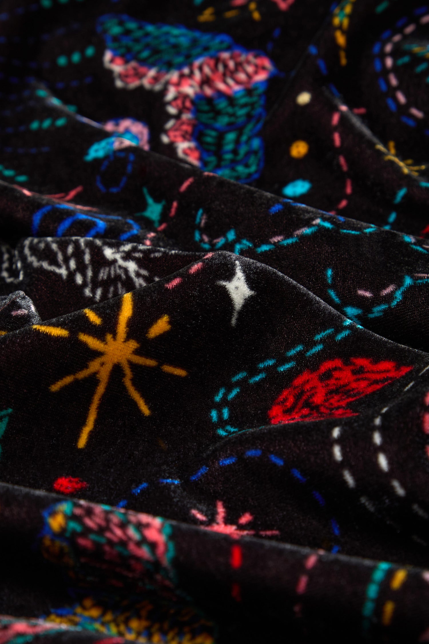 Close-up of the Dream Stitched Print Scarf, a lightweight black scarf adorned with colorful space-themed patterns—stars, planets, and dotted lines—highlighting its folds, texture, and artisanal embroidery.