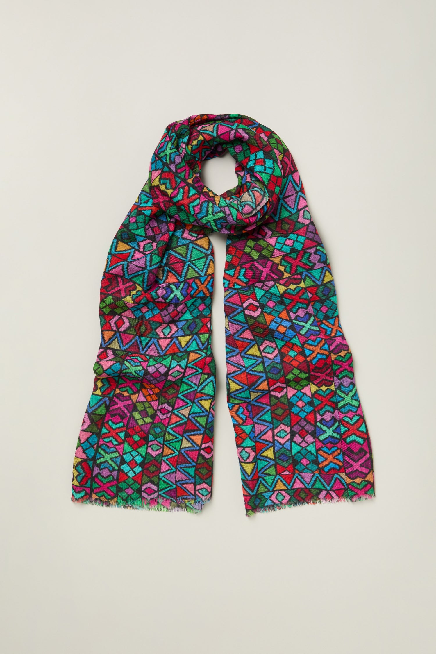 The Peruvian Stitched Print Scarf showcases bright geometric patterns in multiple colors, displayed flat on a light background—a vibrant and lightweight fashion accessory.