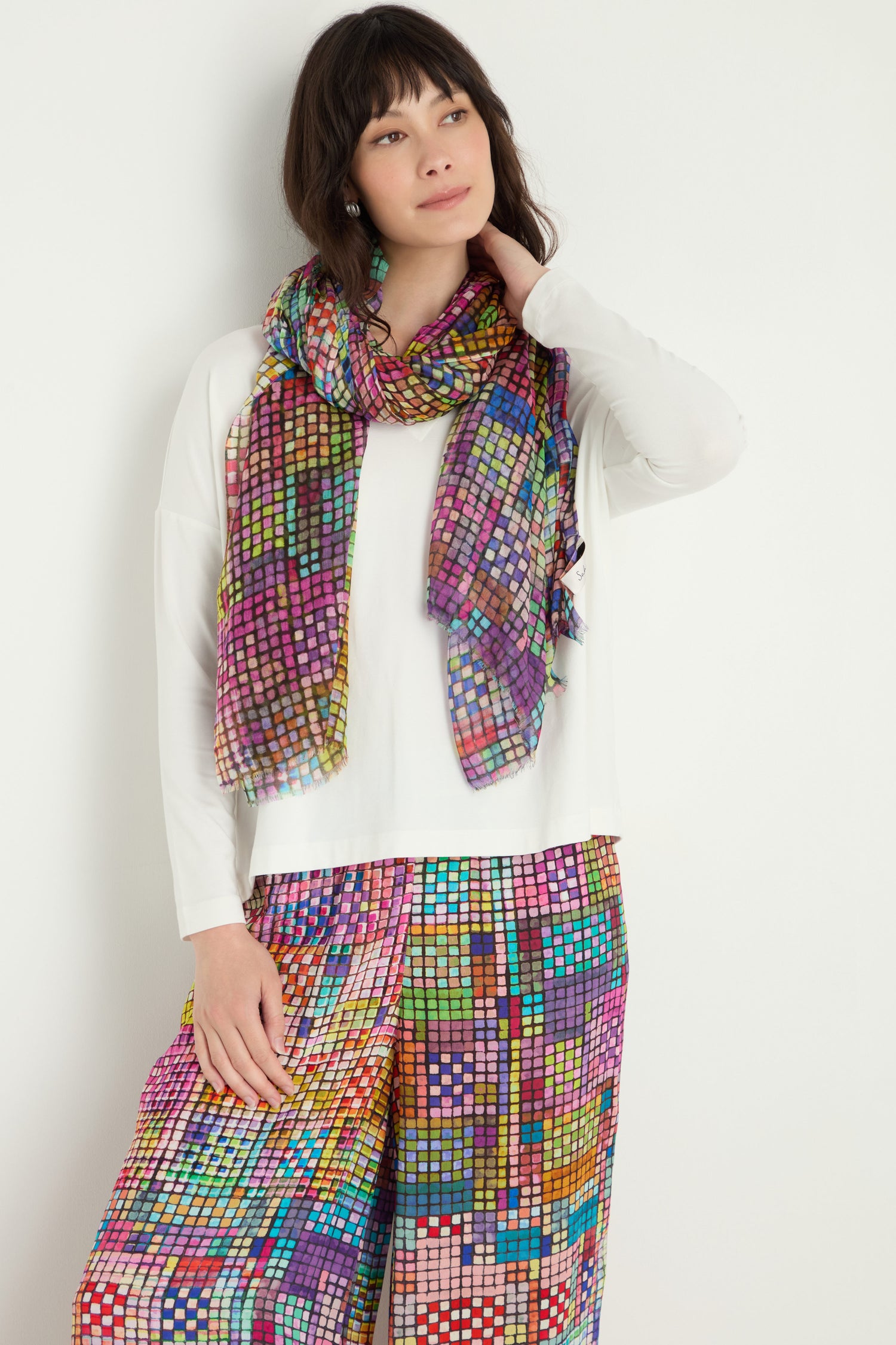 A woman stands against a white background wearing a white long-sleeve top, mosaic-print pants, and the Coloured Glass Tiles Scarf.
