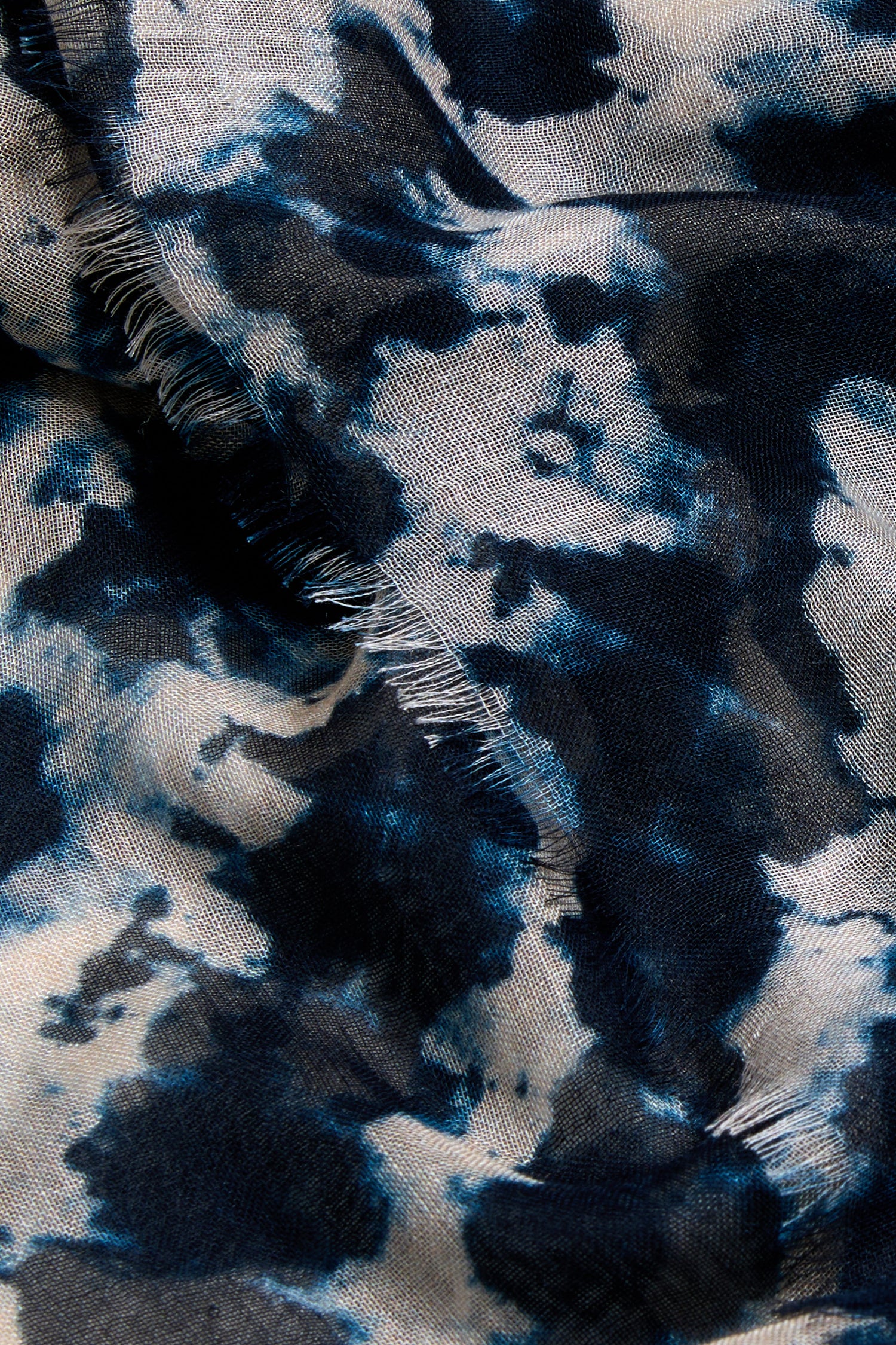 Close-up of the Diamond Tie Dye Scarf, showing its modal silk blend fabric with blue and white diamond patterns and visible frayed edges along a seam.