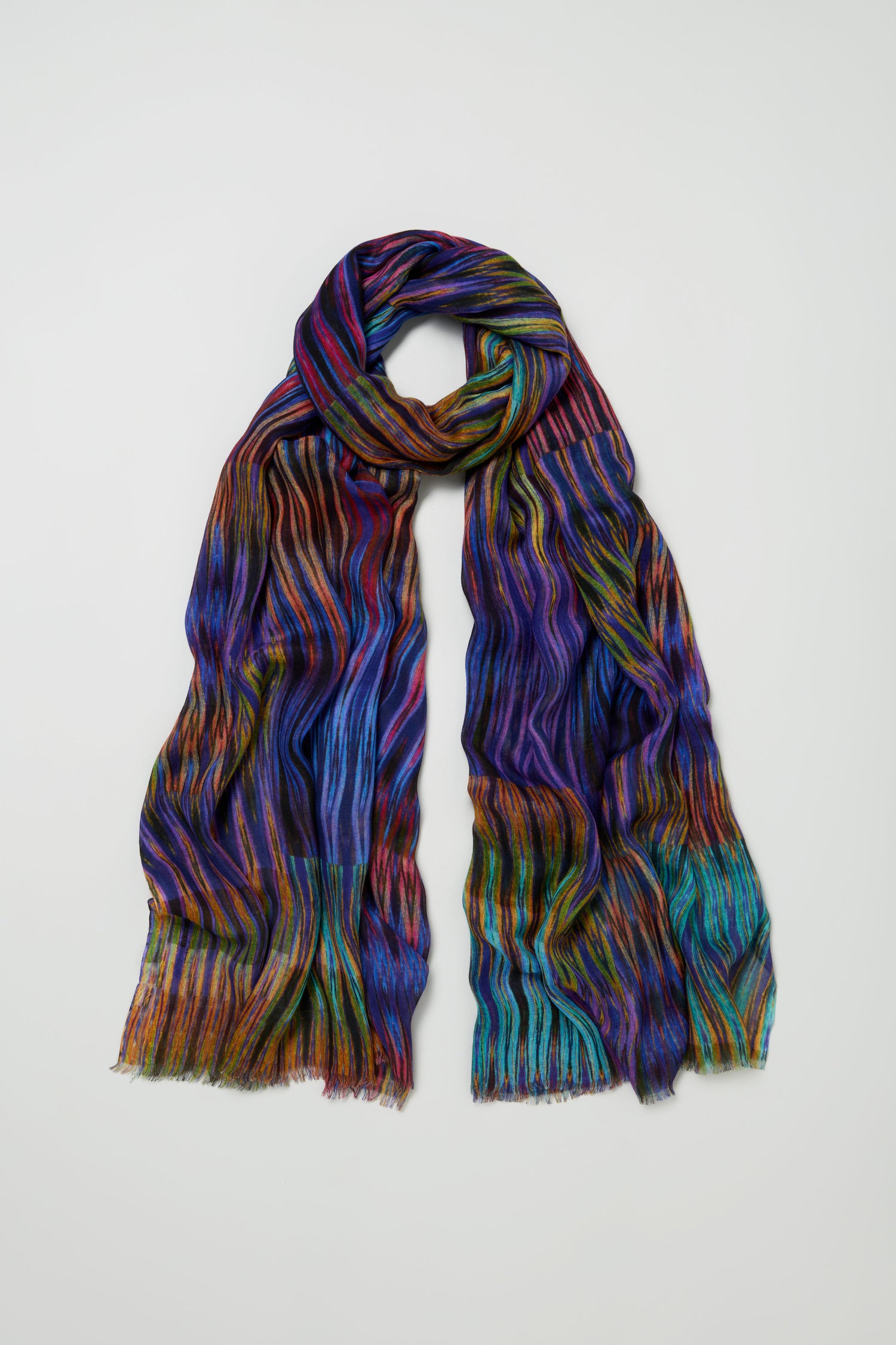 The Vivid Ikat Patchwork Scarf, featuring a wavy striped pattern and fringed ends, is displayed on a plain white background.