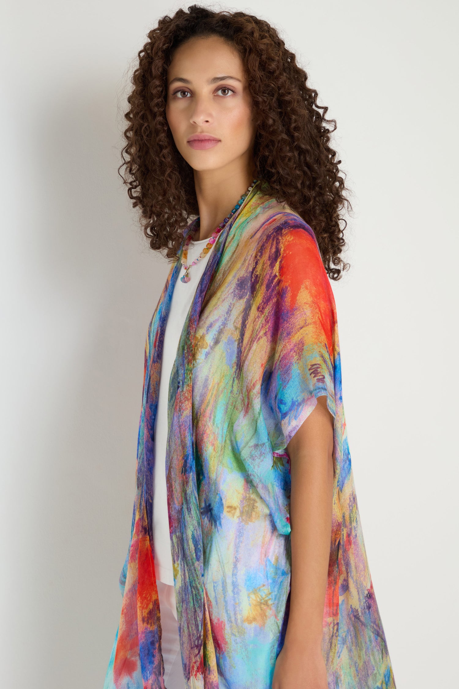 A woman with curly hair wears the Soft Meadow Dreams Kimono over a white outfit, standing against a plain white background.