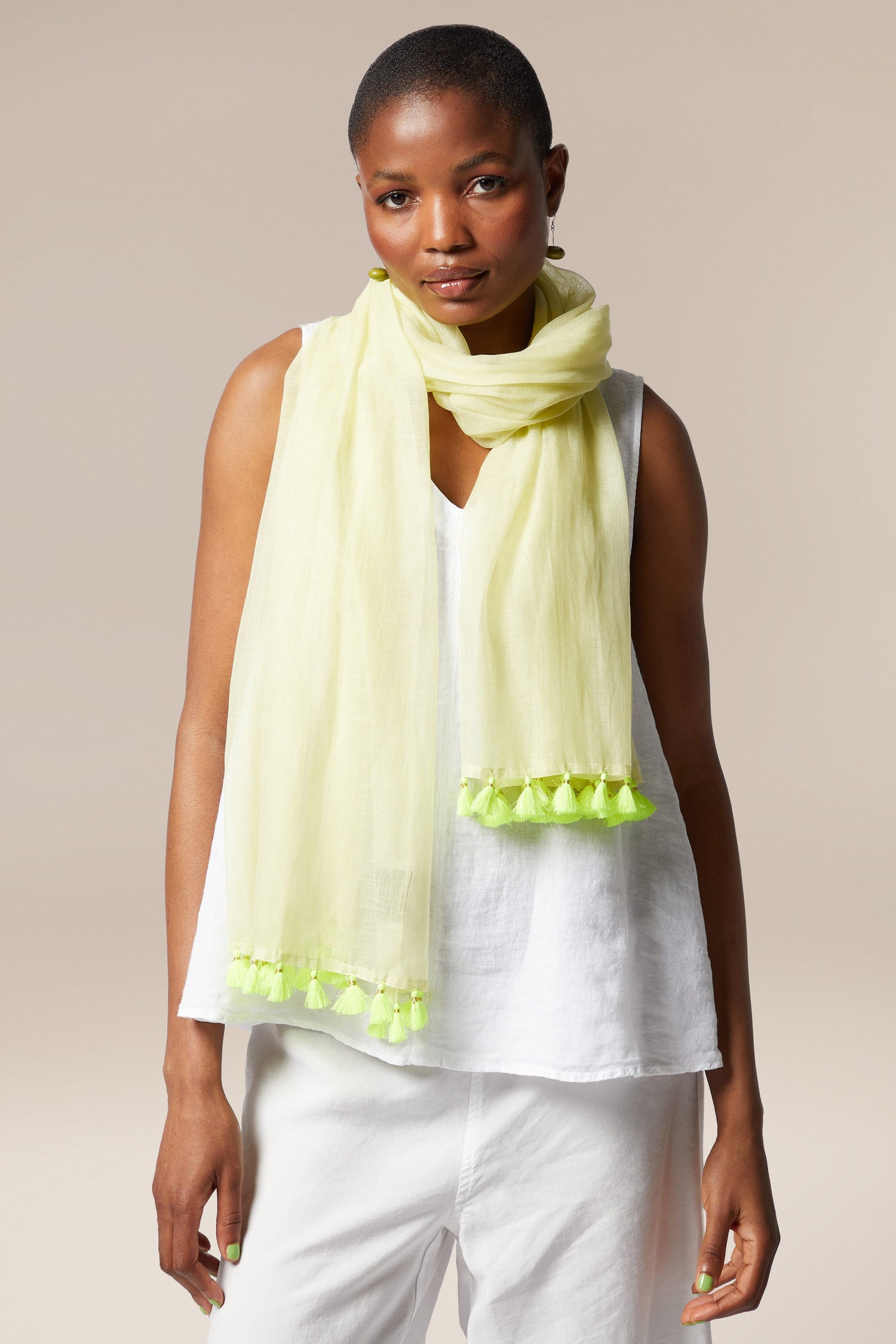A woman wearing a white top and pants with a Neon Tassel Scarf, looking directly at the camera.