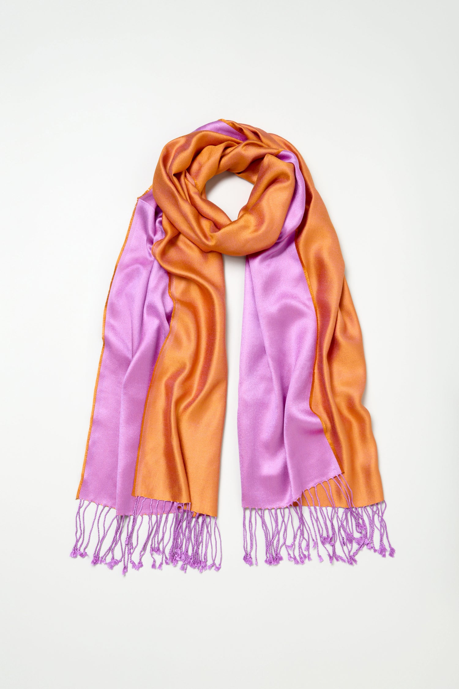 The Two Tone Silk Scarf features orange and pink colorblocked sections, a soft texture, and pink tassels at each end, shown laid flat on a white background.