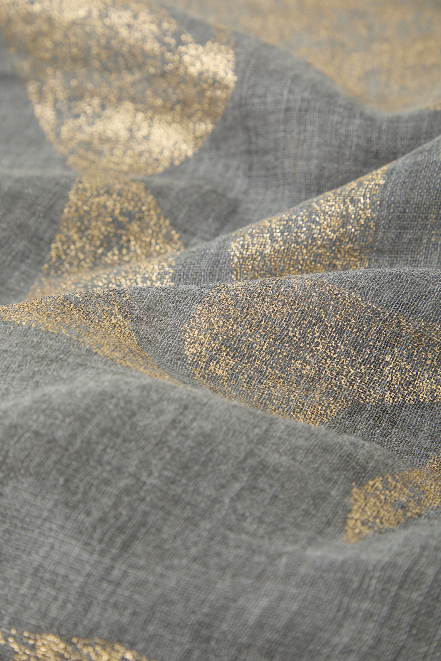 Close-up of Aurelian Cotton Scarf in textured gray, featuring irregular gold metallic patterns. The lightweight surface looks soft with visible folds and creases.