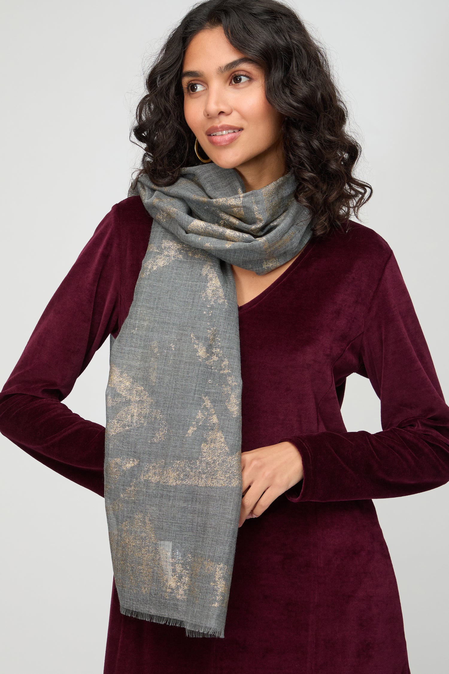 A woman wears the Aurelian Cotton Scarf with gold patterns, draped over a burgundy velvet dress, standing against a plain light background.
