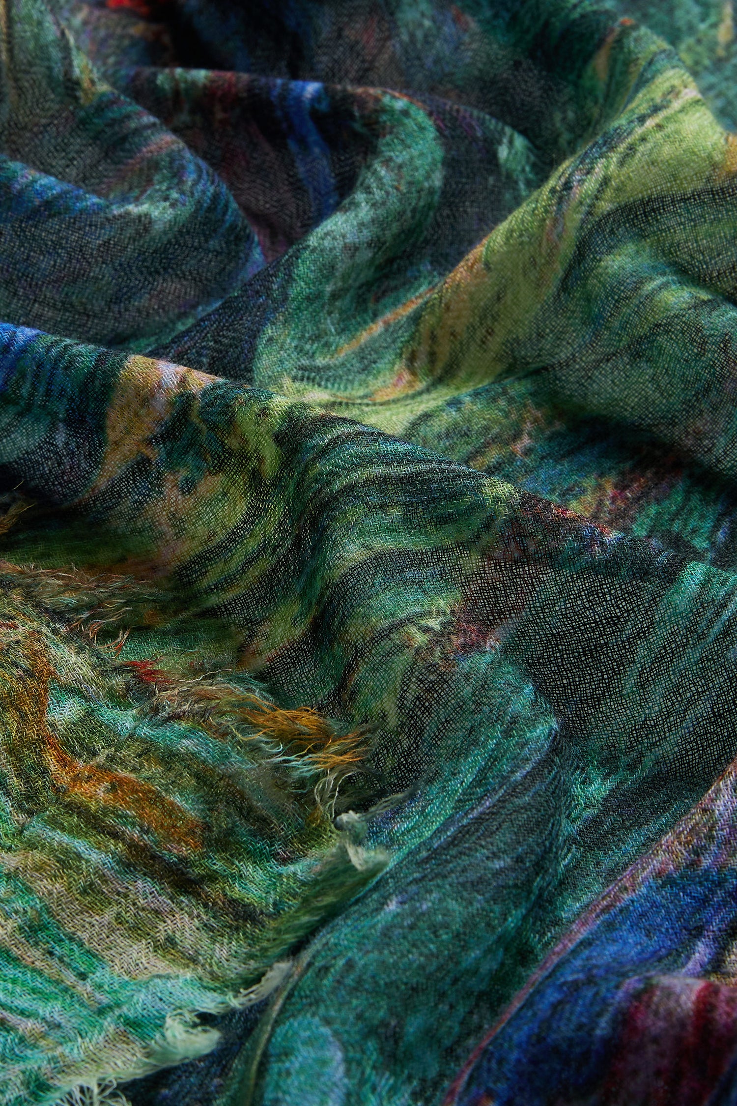 Close-up of the Painter's Landscape Wool Scarf, showcasing textured wool fibers and vibrant multicolored patterns in green, blue, and yellow with a slightly frayed edge.