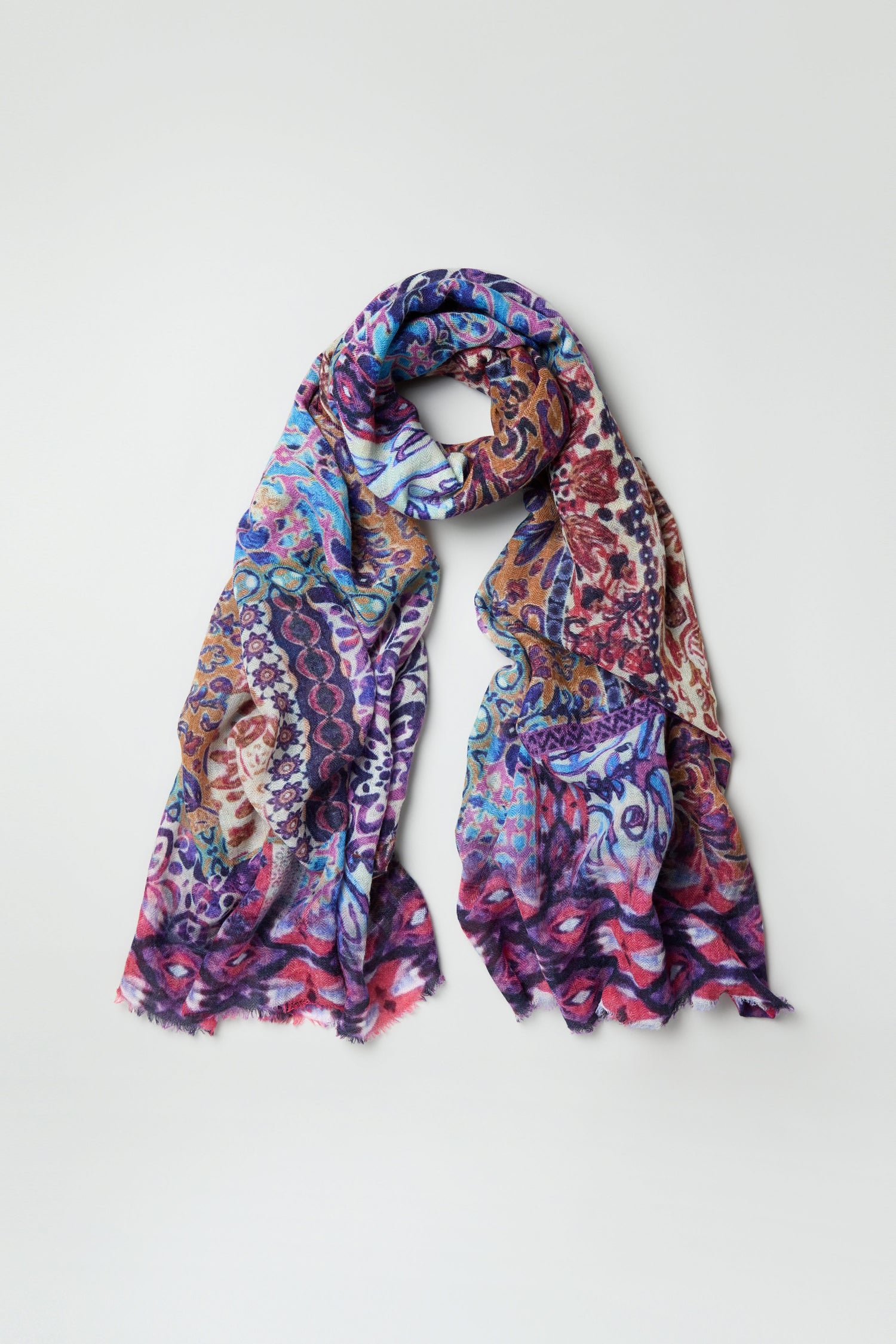 The Patchwork Mural Print Wool Scarf features an oversized design with colorful paisley and abstract patterns in blue, purple, red, and gold tones—adding bold visual flair when laid flat on a light background.