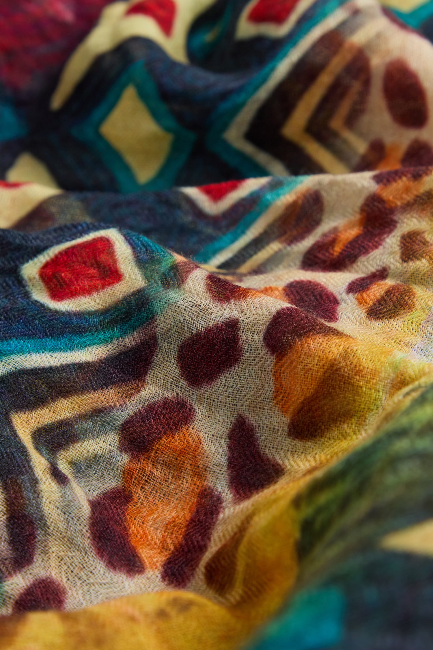 Close-up of a textured fabric from the Savannah Print Wool Scarf, featuring oversized geometric and abstract patterns in vibrant red, blue, yellow, and brown.