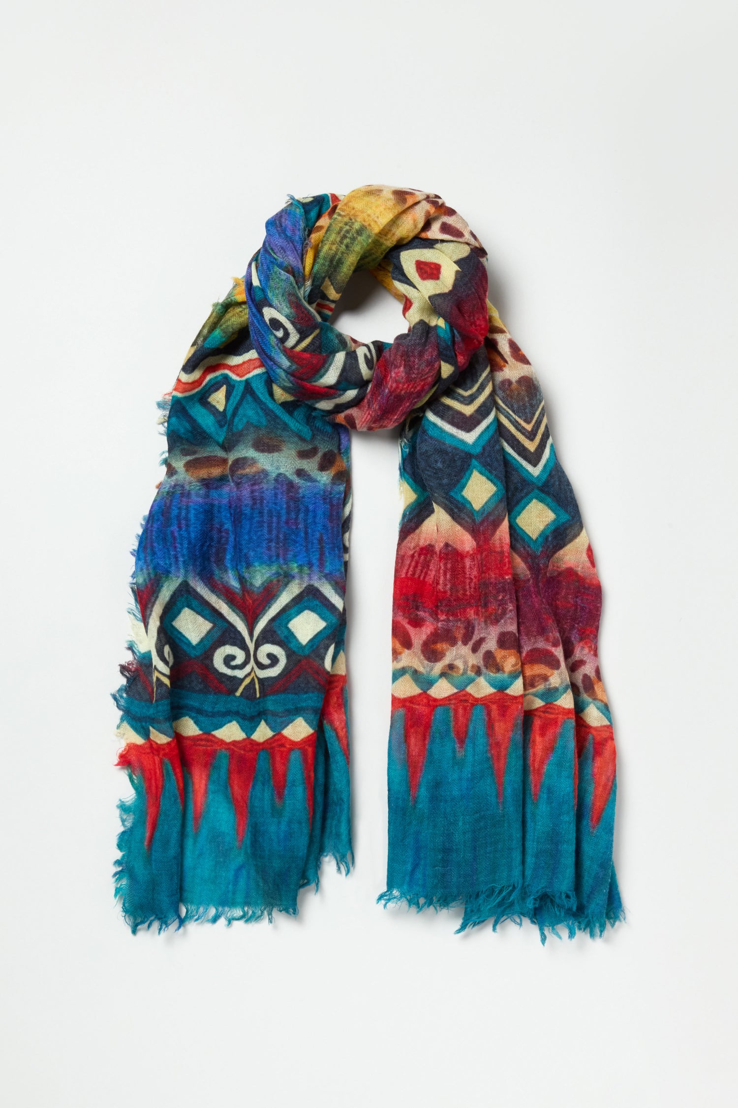 The Savannah Print Wool Scarf features vibrant geometric and animal patterns in blue, red, yellow, and brown, set against a white background.