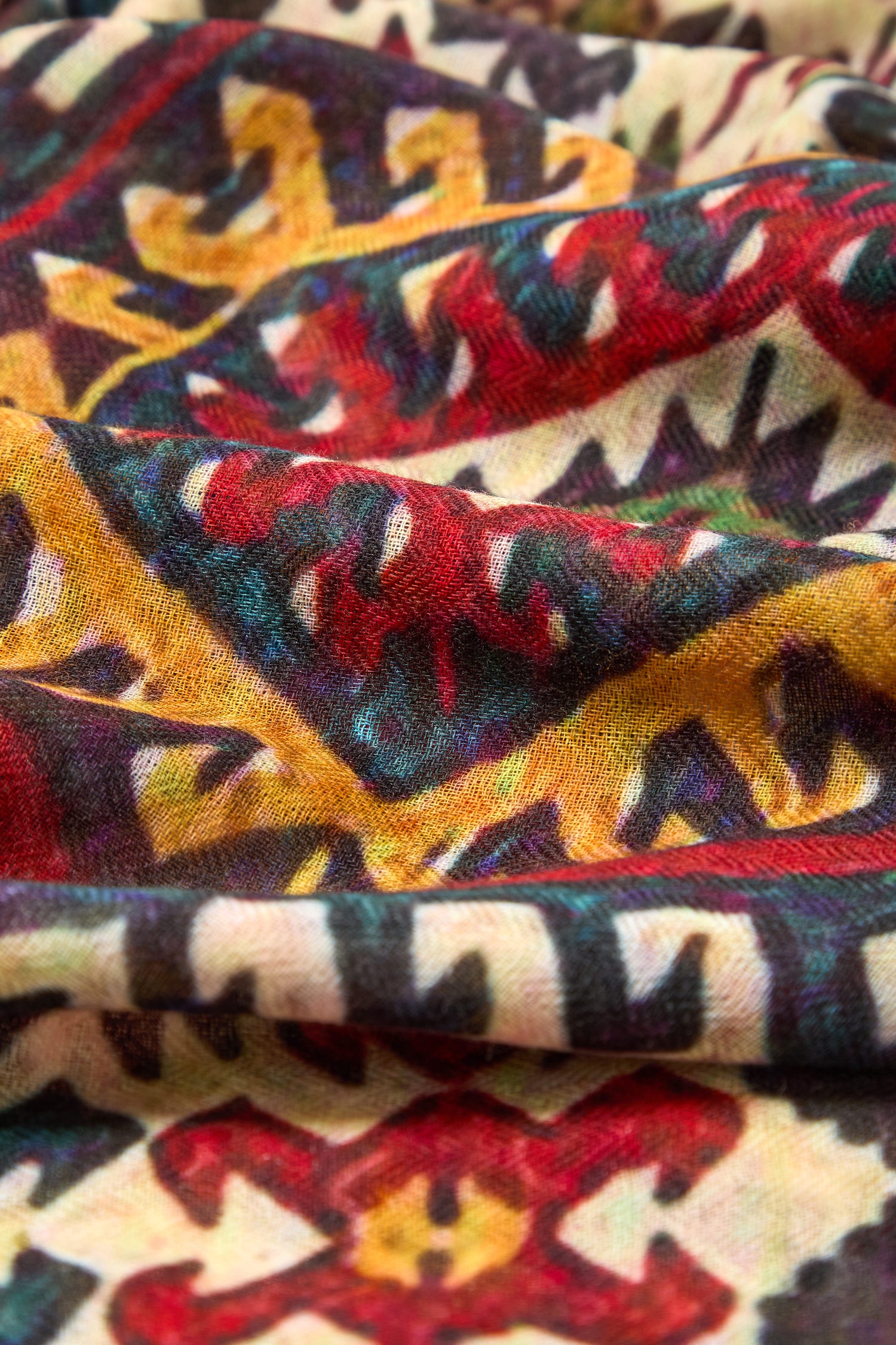 Close-up of the Tapestry Wool Scarf, showcasing red, yellow, black, and blue geometric and abstract patterns with visible texture and folds.