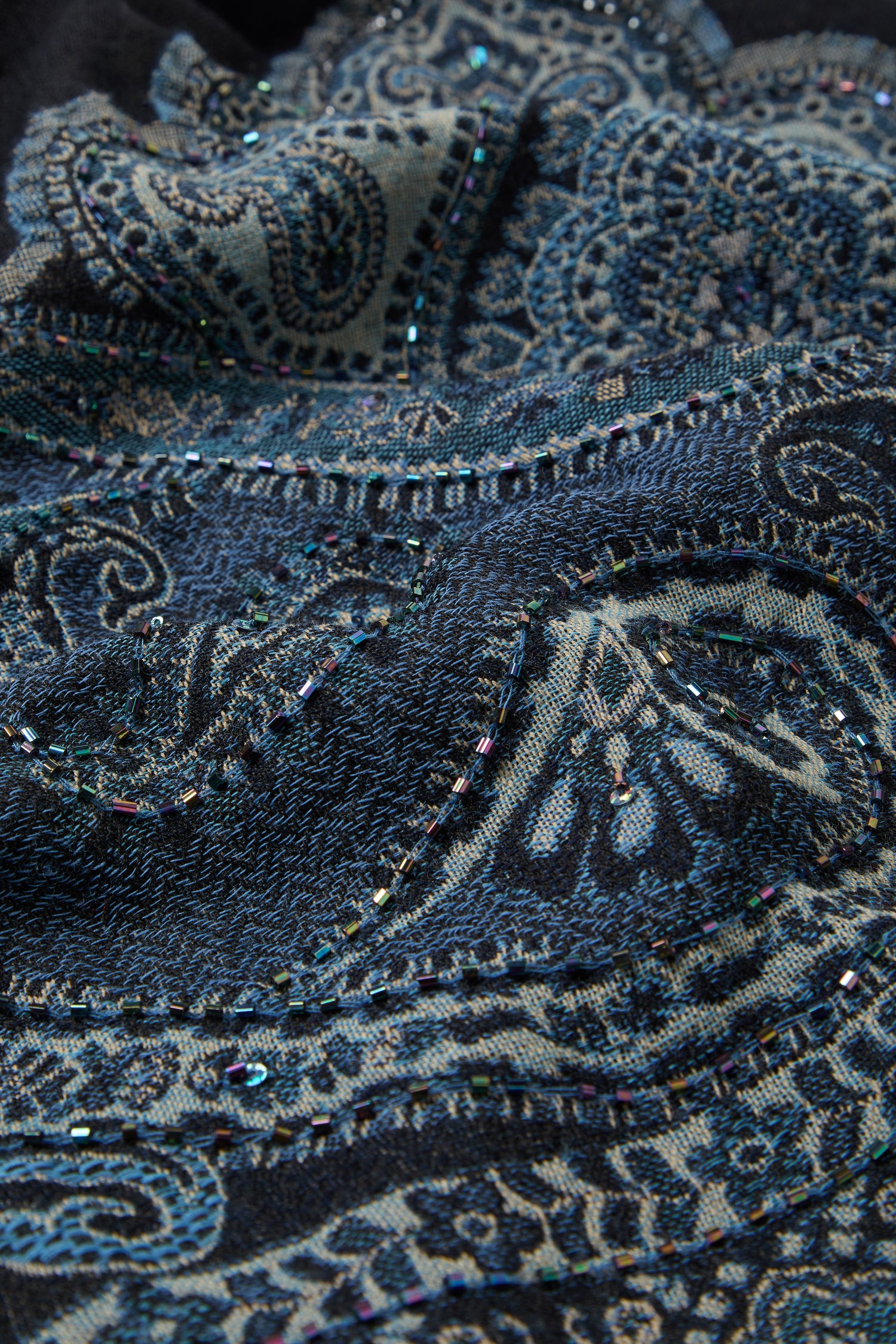 Close-up of the Opulent Paisley Wool Scarf in dark blue and black wool, adorned with intricate paisley patterns and small iridescent beads sewn into the design.