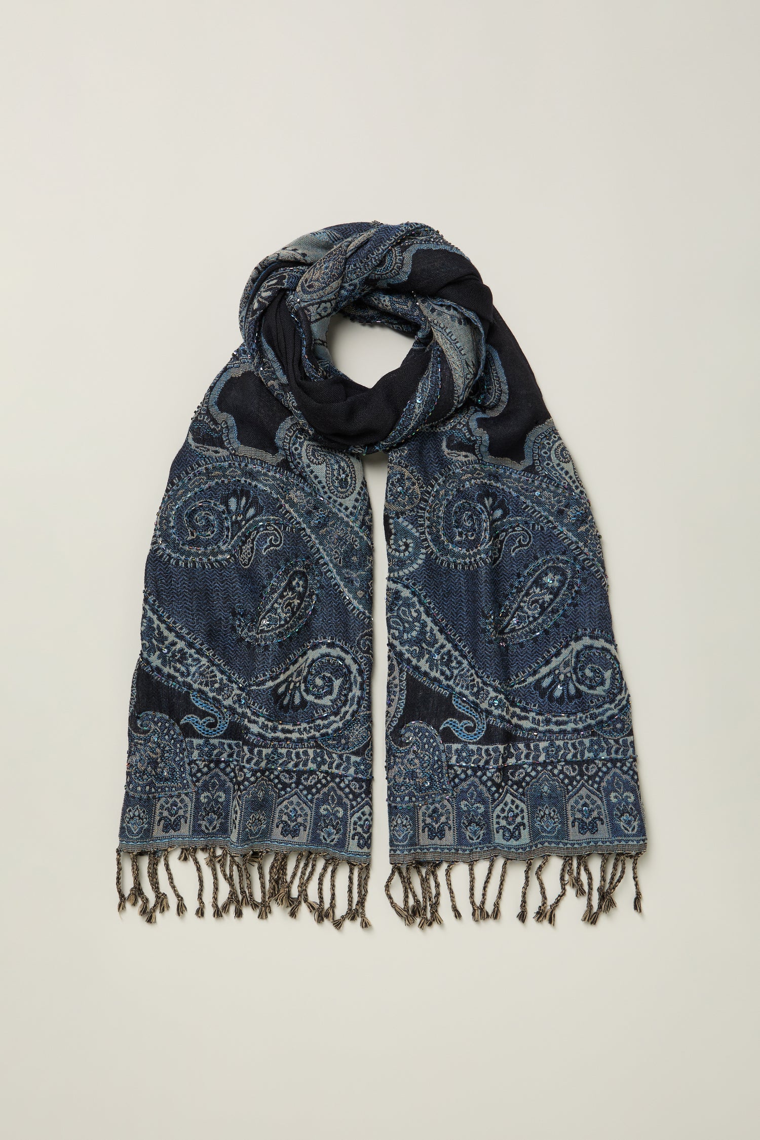 The Opulent Paisley Wool Scarf, featuring blue paisley patterns and fringed ends, is displayed against a neutral background and adds elegance to any outfit.