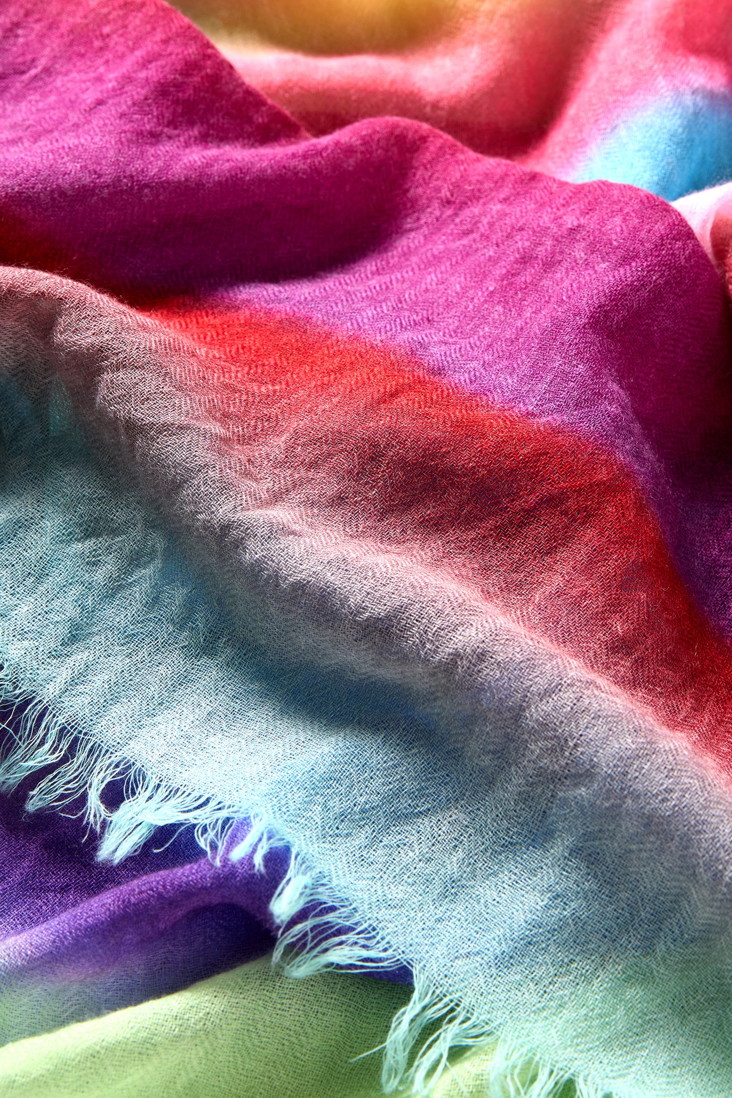 The Horizon Stripe Wool Scarf features soft, textured wool with a lightweight weave, visible frayed edges, and a vibrant ombre design in pink, red, blue, green, and purple for effortless style.