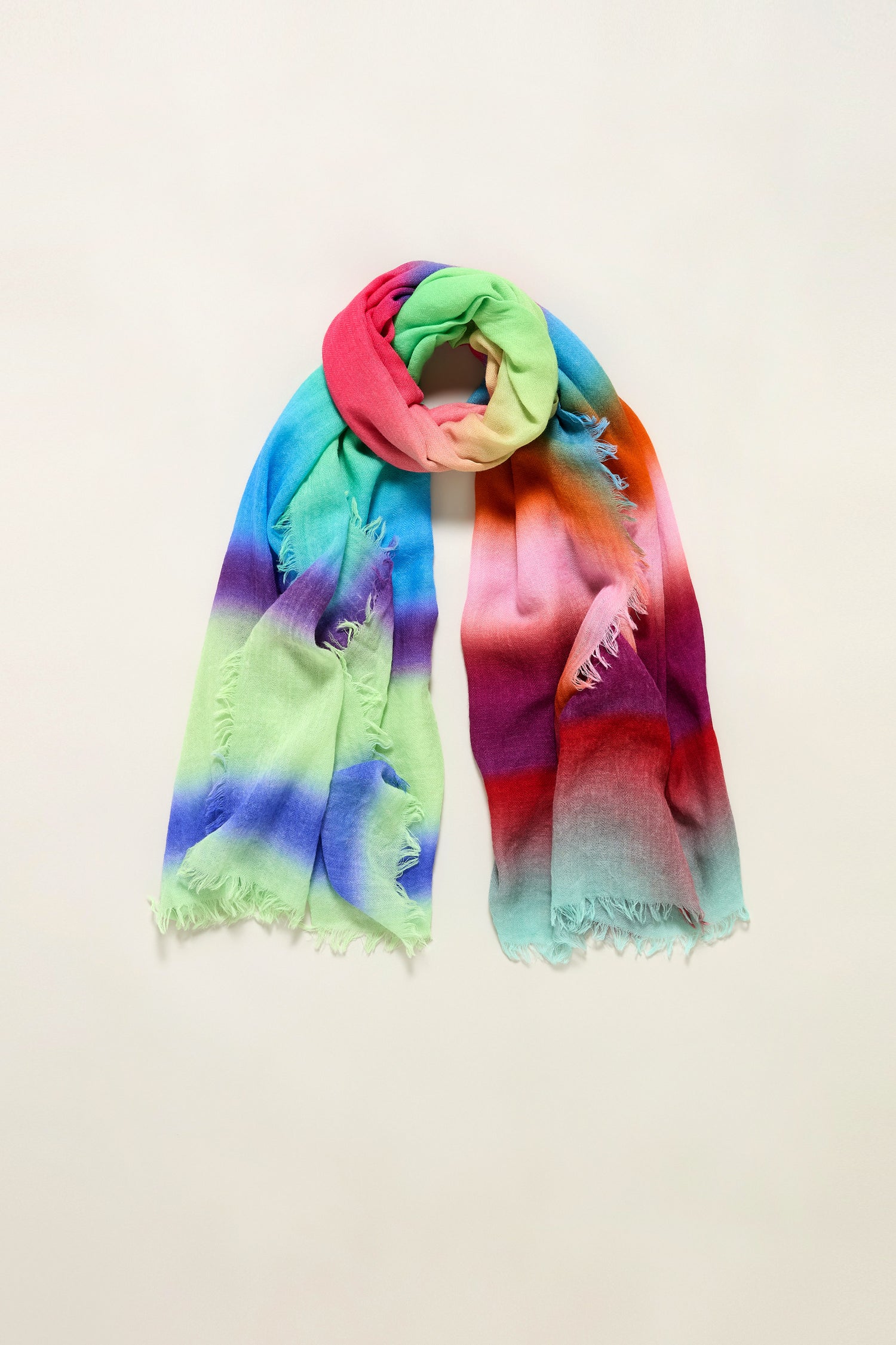 The Horizon Stripe Wool Scarf is a rectangular pure wool scarf with frayed edges, featuring a lightweight weave and a green, pink, blue, purple, red, and orange gradient tie-dye ombre design.