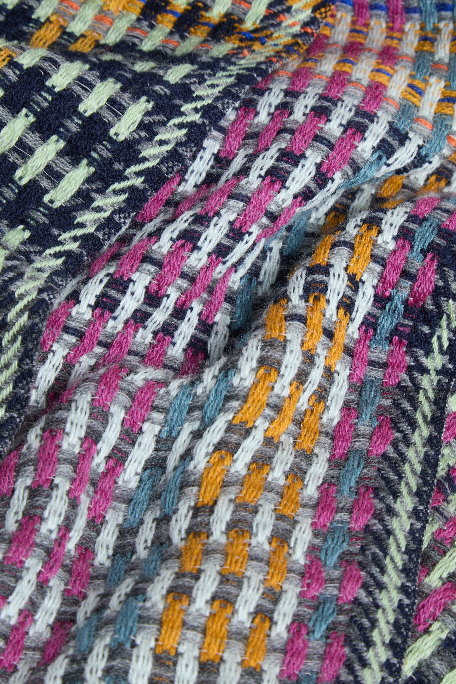 Close-up of the Checkerboard Scarf, a wool-blend accessory featuring a grid pattern in pink, yellow, blue, gray, and cream threads against a dark background. This scarf offers lightweight warmth with its textured and layered woven design.