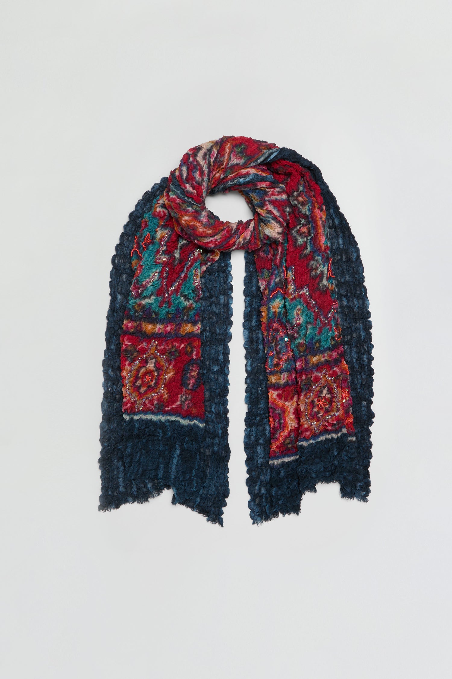 The Crushed Sequin Detail Wool Scarf is displayed flat on a white background, showcasing its vibrant red, blue, and green pattern. The textured, uneven ends and subtle sequin embellishments add shimmering accents, highlighting the lively design of this eye-catching accessory.