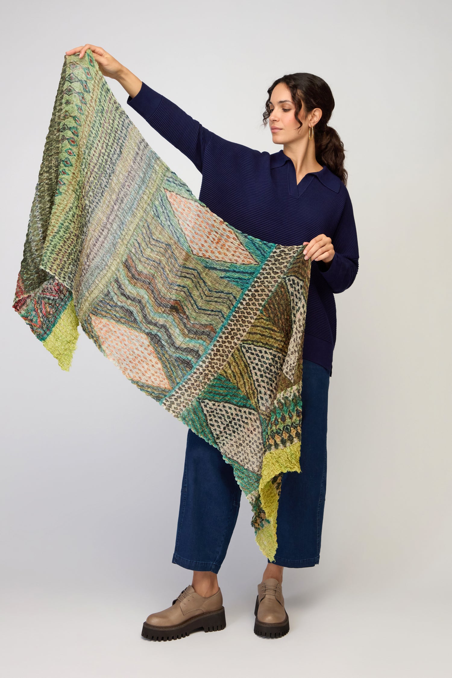A woman in a navy top and wide-leg jeans holds out the Crushed Digital Print Wool Scarf, showcasing its bold, vibrant design against a plain background.