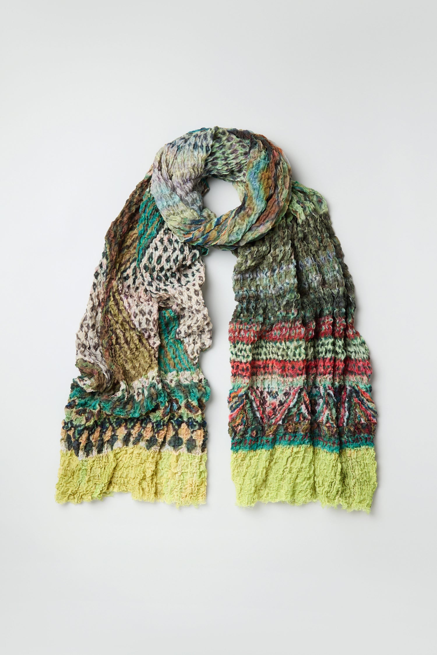 The Crushed Digital Print Wool Scarf, oversized and multicolored with textured patterns in green, yellow, red, blue, and beige, is displayed flat on a plain background.