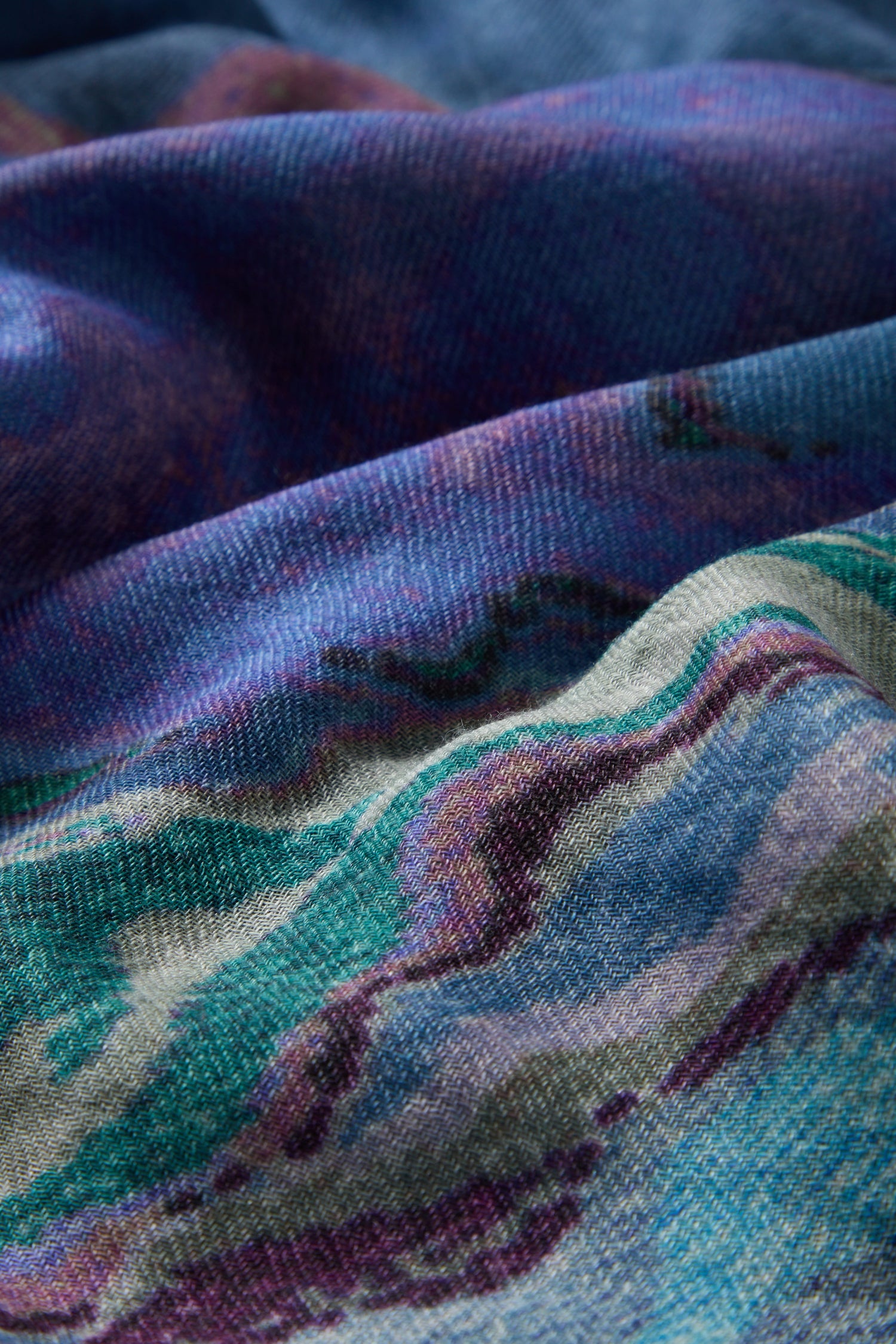 Close-up of the Agate Wool Scarf, showcasing its textured fabric with a multicolored abstract pattern in shades of blue, purple, teal, and cream. The woven details and folds highlight the Indian textile's agate-inspired print, giving it a unique artistic touch reminiscent of luxurious wool-silk accessories.