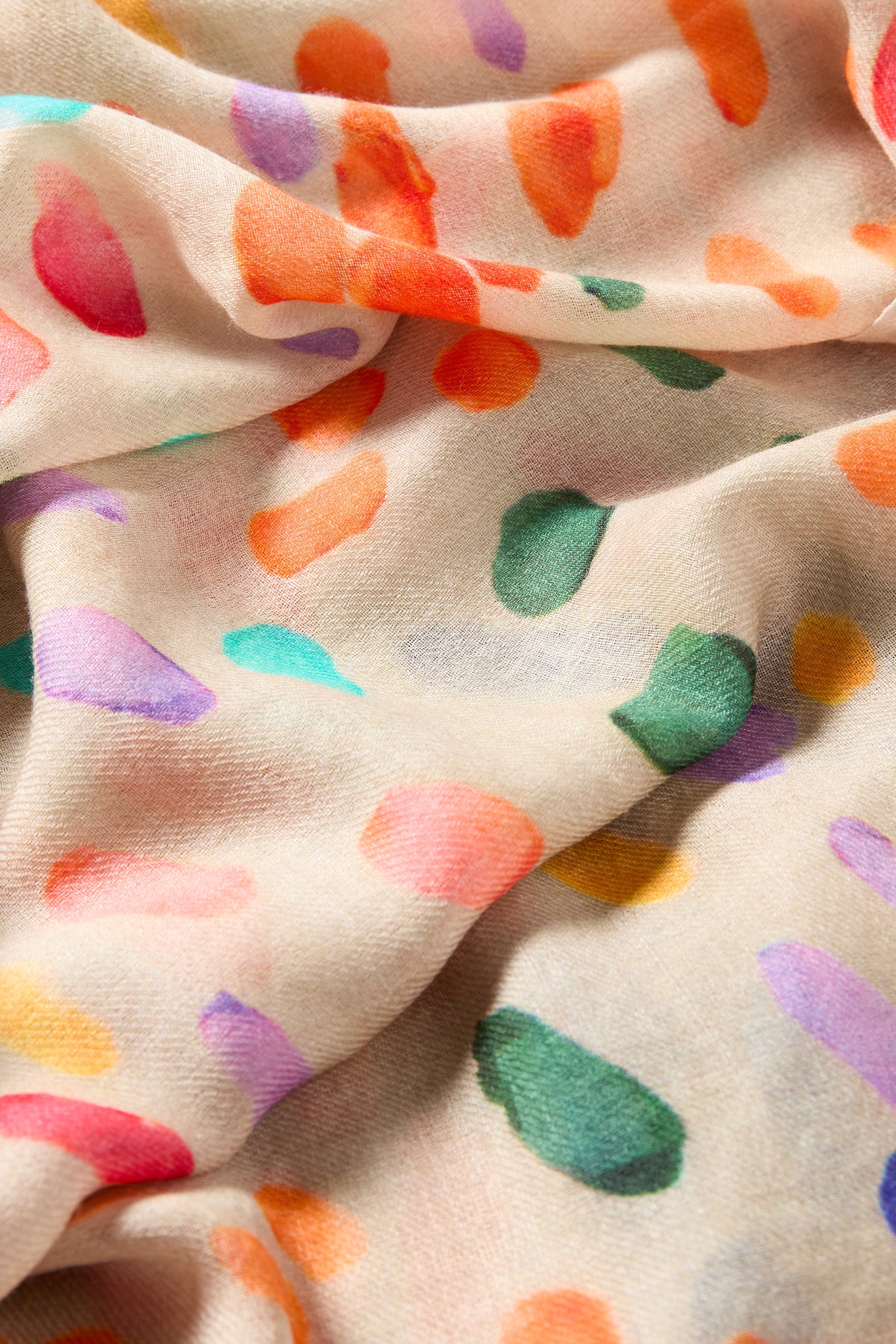 Close-up of the Artful Dots Wool Silk Scarf in light beige, showcasing colorful irregular orange, green, purple, and red spots on a soft wool-silk blend with a lightly wrinkled texture.