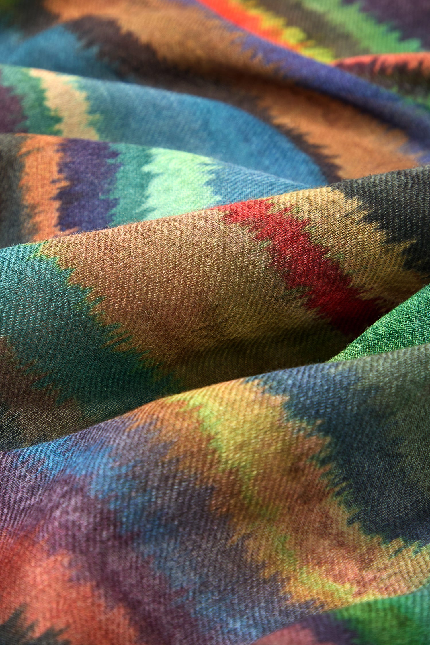Close-up of the Fluid Stripe Wool Scarf featuring a vibrant zigzag pattern in green, blue, orange, brown, and red tones, highlighting its rich texture and gentle folds.