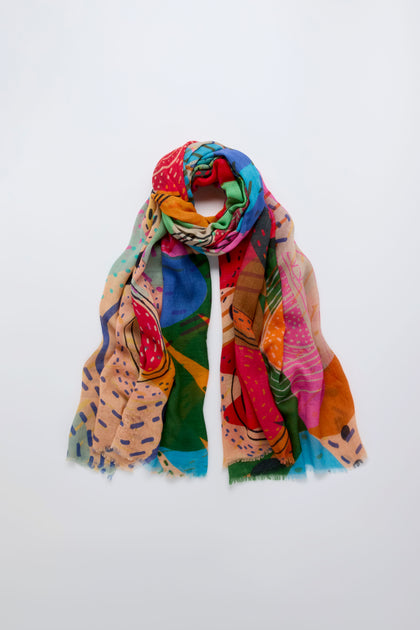 The Tutti Frutti Wool Twill Scarf, featuring a vibrant abstract pattern, is displayed flat and loosely rolled on a plain white background.