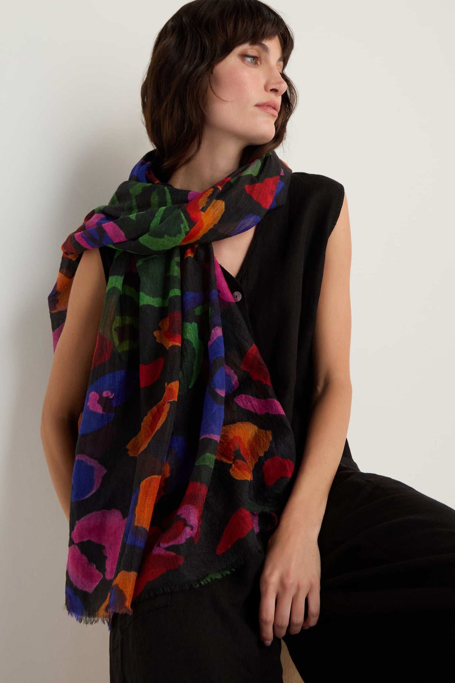 A woman poses against a plain light background, wearing a sleeveless black outfit accessorized with the Painted Pansy Wool Scarf.