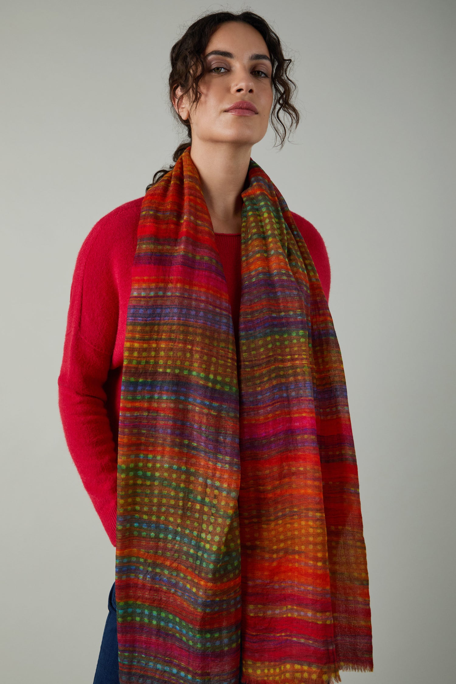 A person wearing a red sweater and the Sundown Stripe Wool Scarf stands against a plain light gray background.