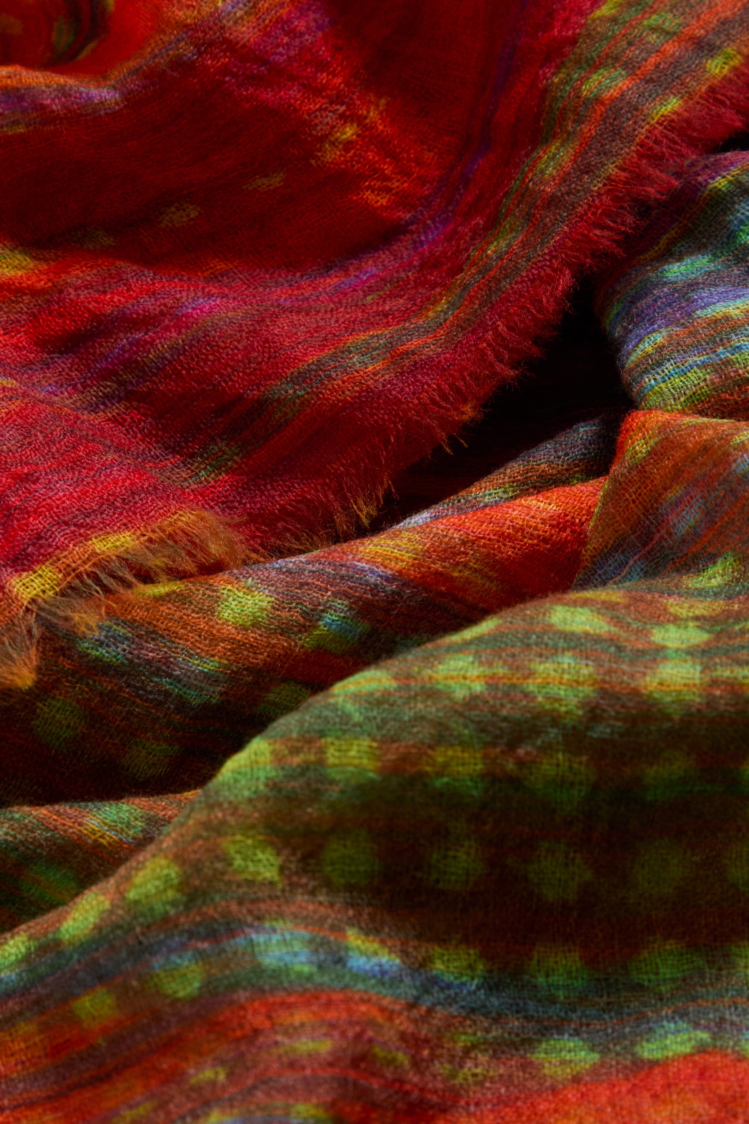 Close-up of the Sundown Stripe Wool Scarf, showcasing its textured wool with vibrant red, green, and yellow stripes and frayed edges.