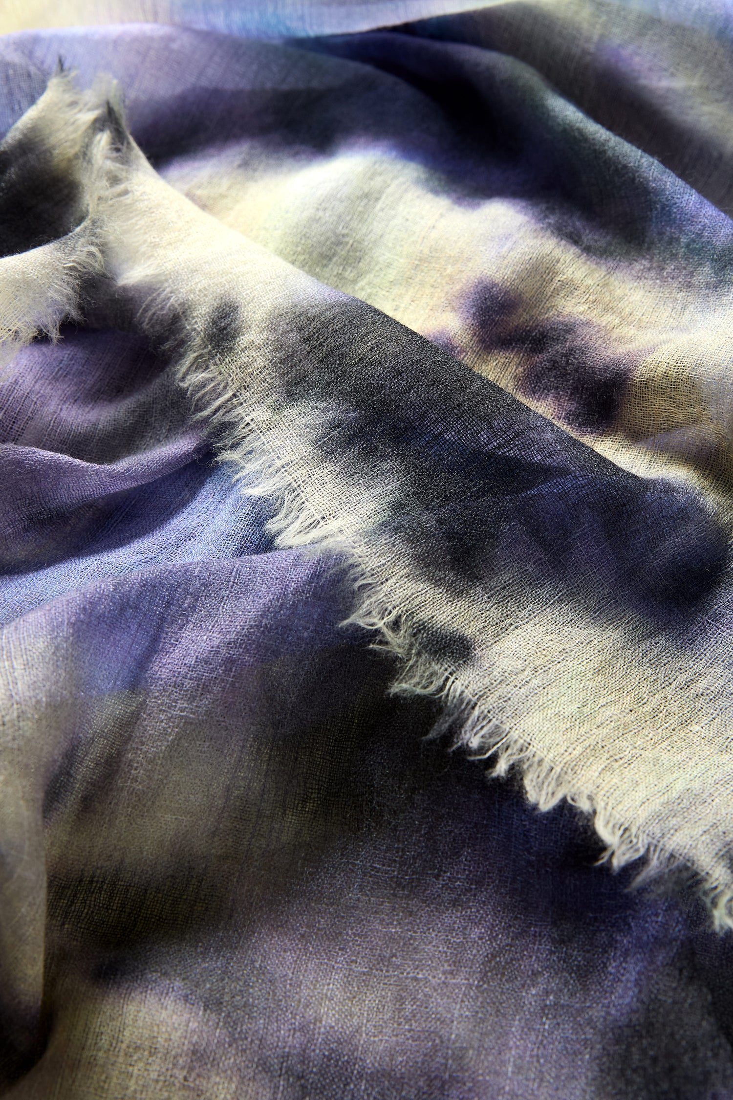 Close-up of the Spiral Tie Dye Wool Scarf, made from pure wool with a frayed edge and a tie-dye pattern in purple, blue, and cream shades.