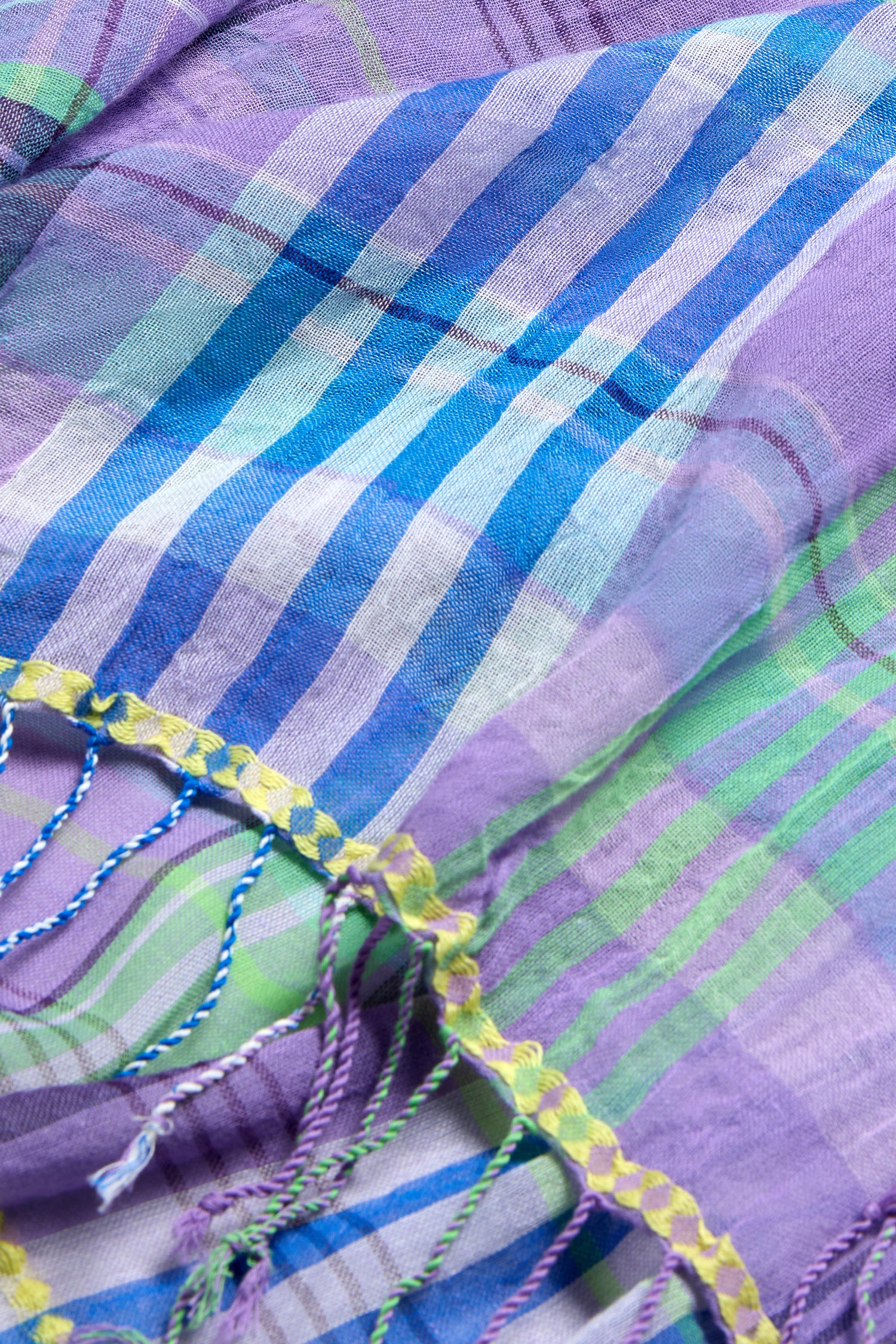 Close-up of the Check Stitch Cotton Scarf, a lightweight, breathable cotton accessory in colorful plaid with blue, green, and purple stripes, finished with tasseled yellow and blue threads along the edge.