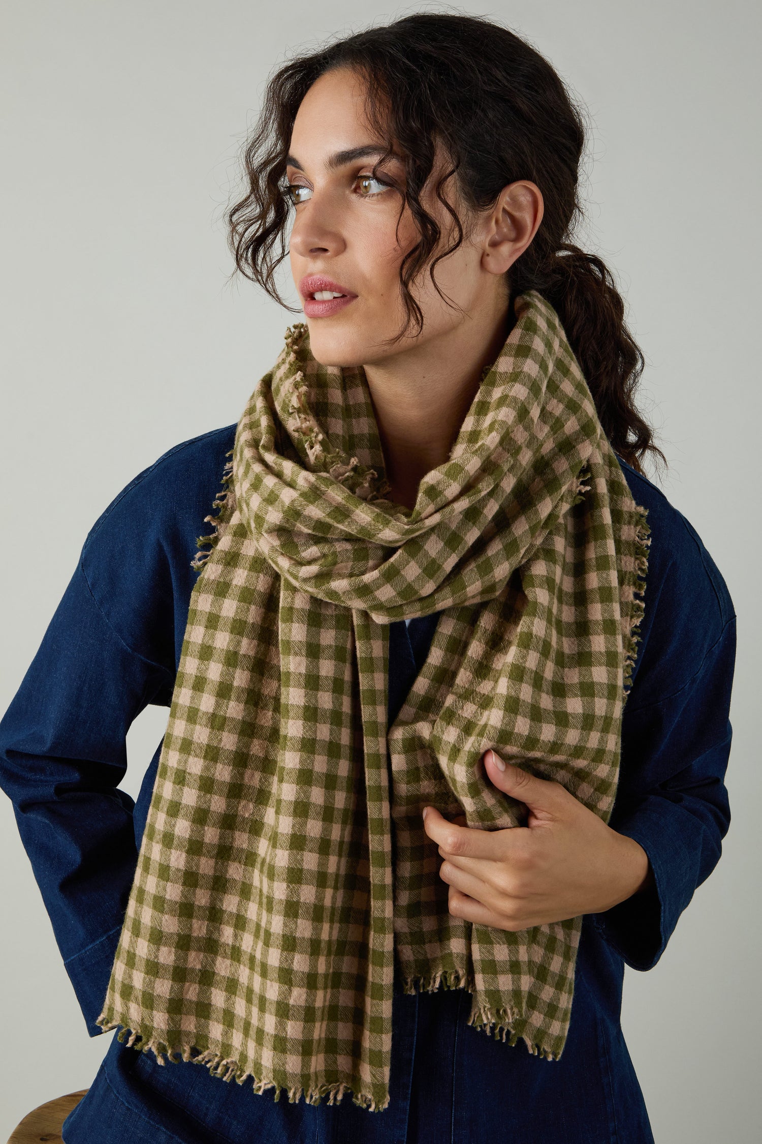 A woman in a dark blue top wears the Boiled Wool Gingham Check Scarf with large green and beige checks, looking to the side against a plain background.