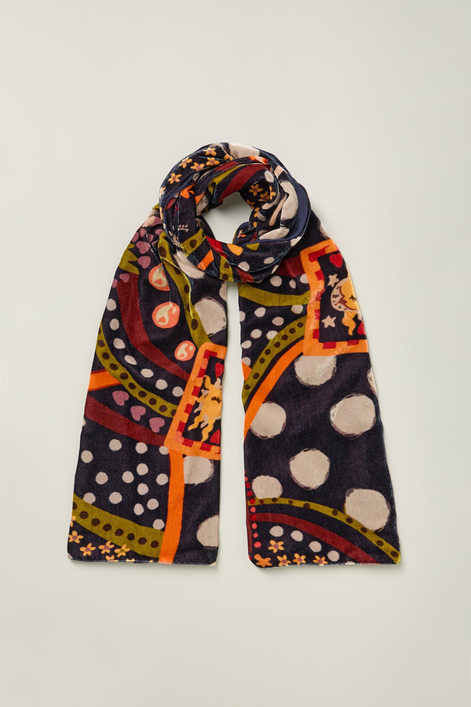 The Hera Velvet Scarf is a rectangular accessory with a colorful abstract pattern, featuring polka dots and geometric shapes in navy, orange, red, green, and beige—perfect for eveningwear.