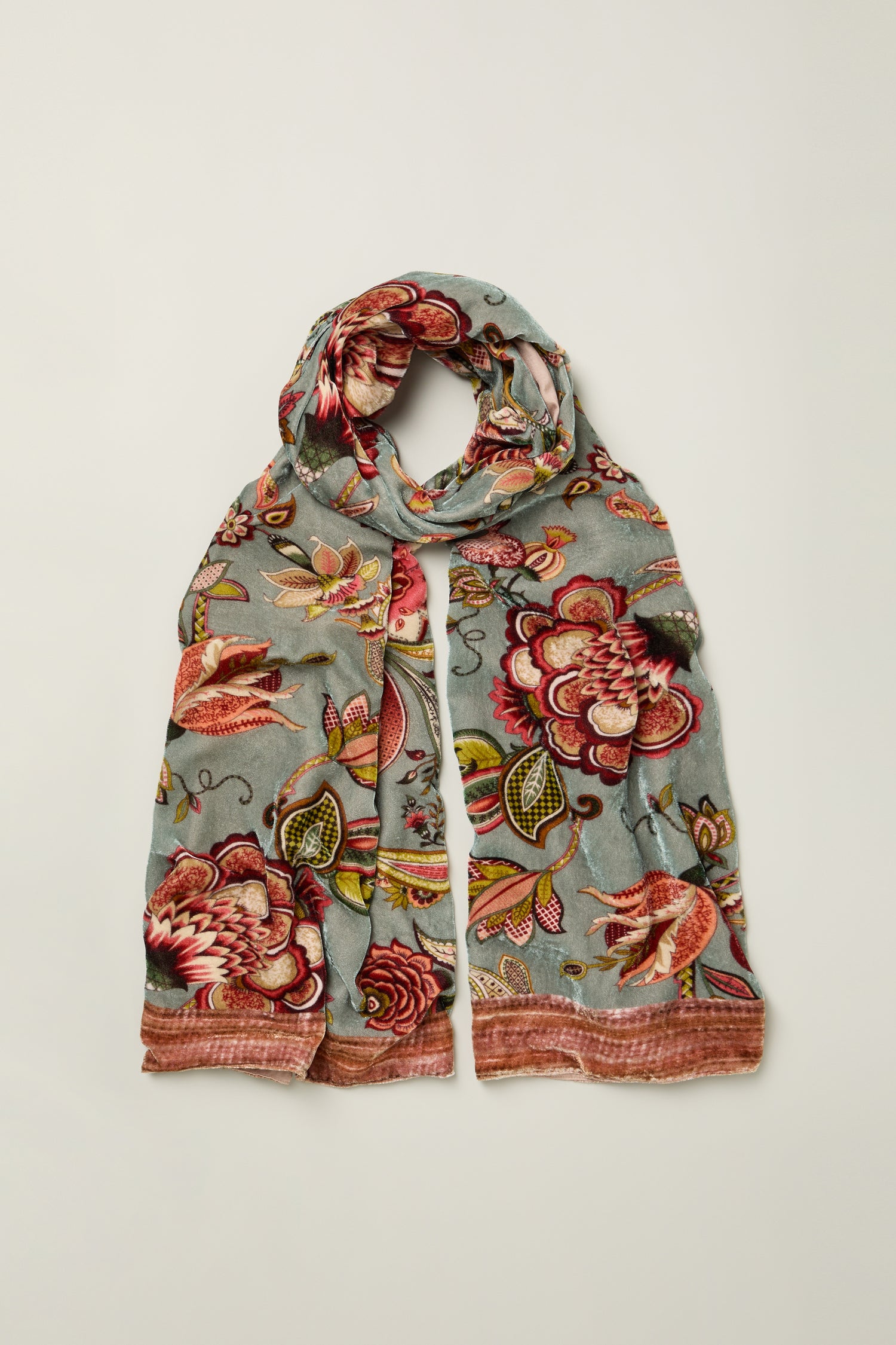 The In Bloom Velvet Scarf features a floral pattern in red, pink, green, and yellow on a light blue background. Neatly folded on a plain surface, it's the perfect statement accessory for any outfit.