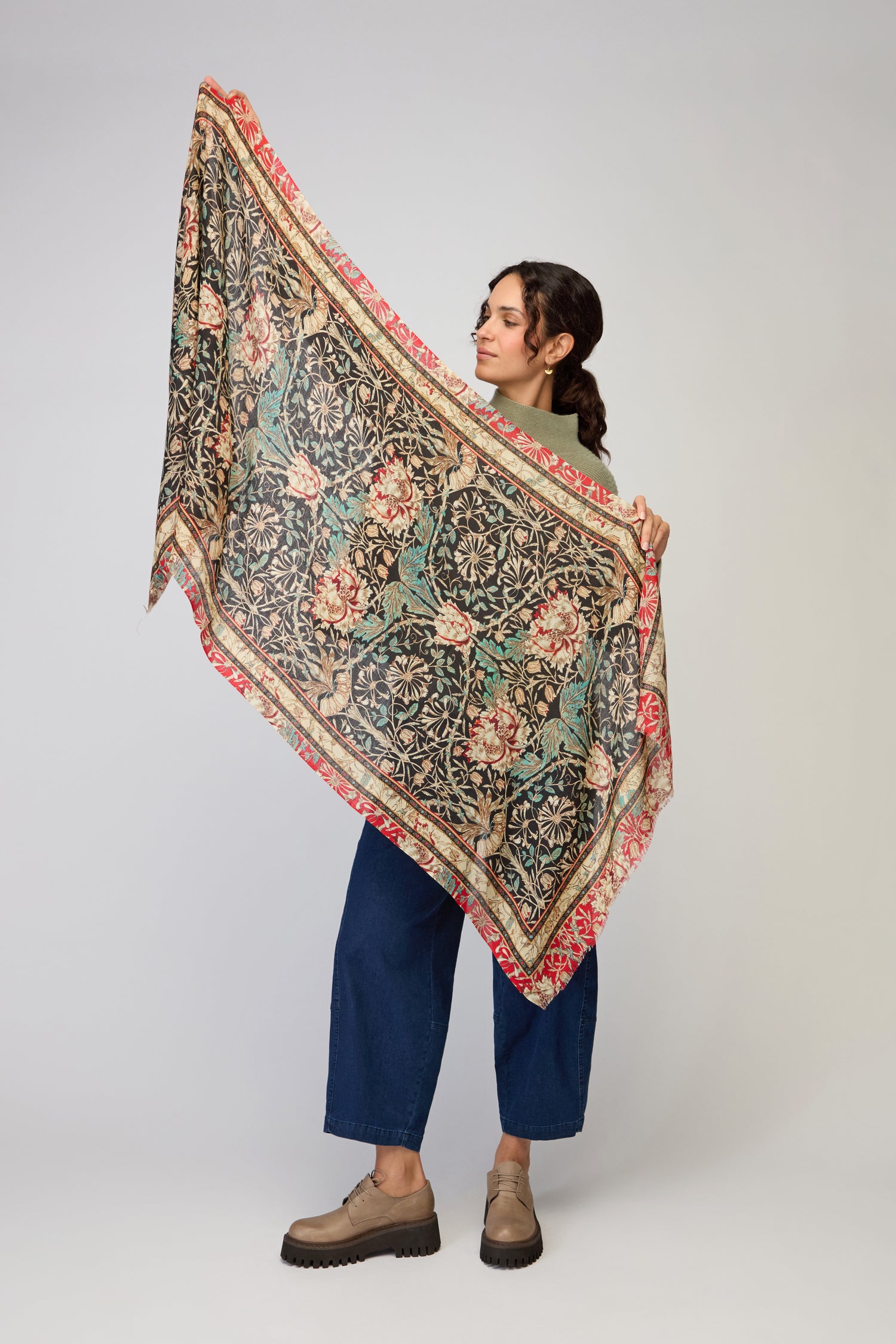 A woman holds up the Ornamental Floral Wool Mix Scarf, featuring geometric designs, against a plain background.