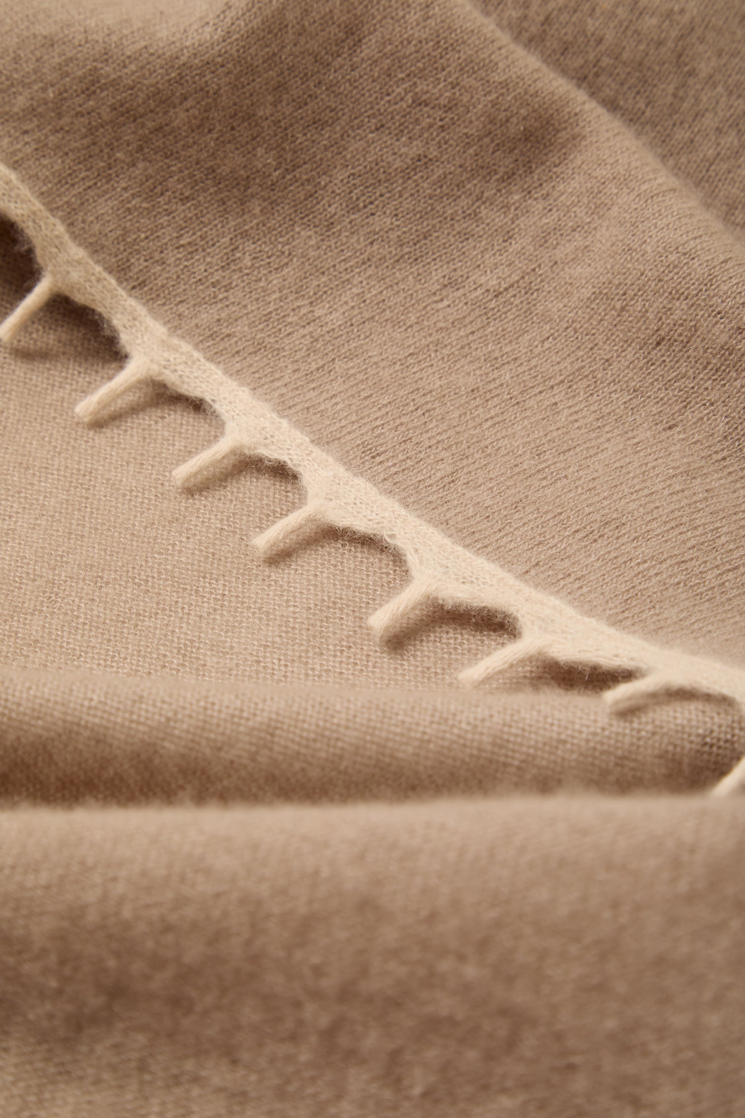Close-up of the Contrast Trim Cream Cashmere Scarf, highlighting its beige cashmere fabric with a visible seam, large evenly spaced stitches, and a subtle contrast trim detailing along the edge.