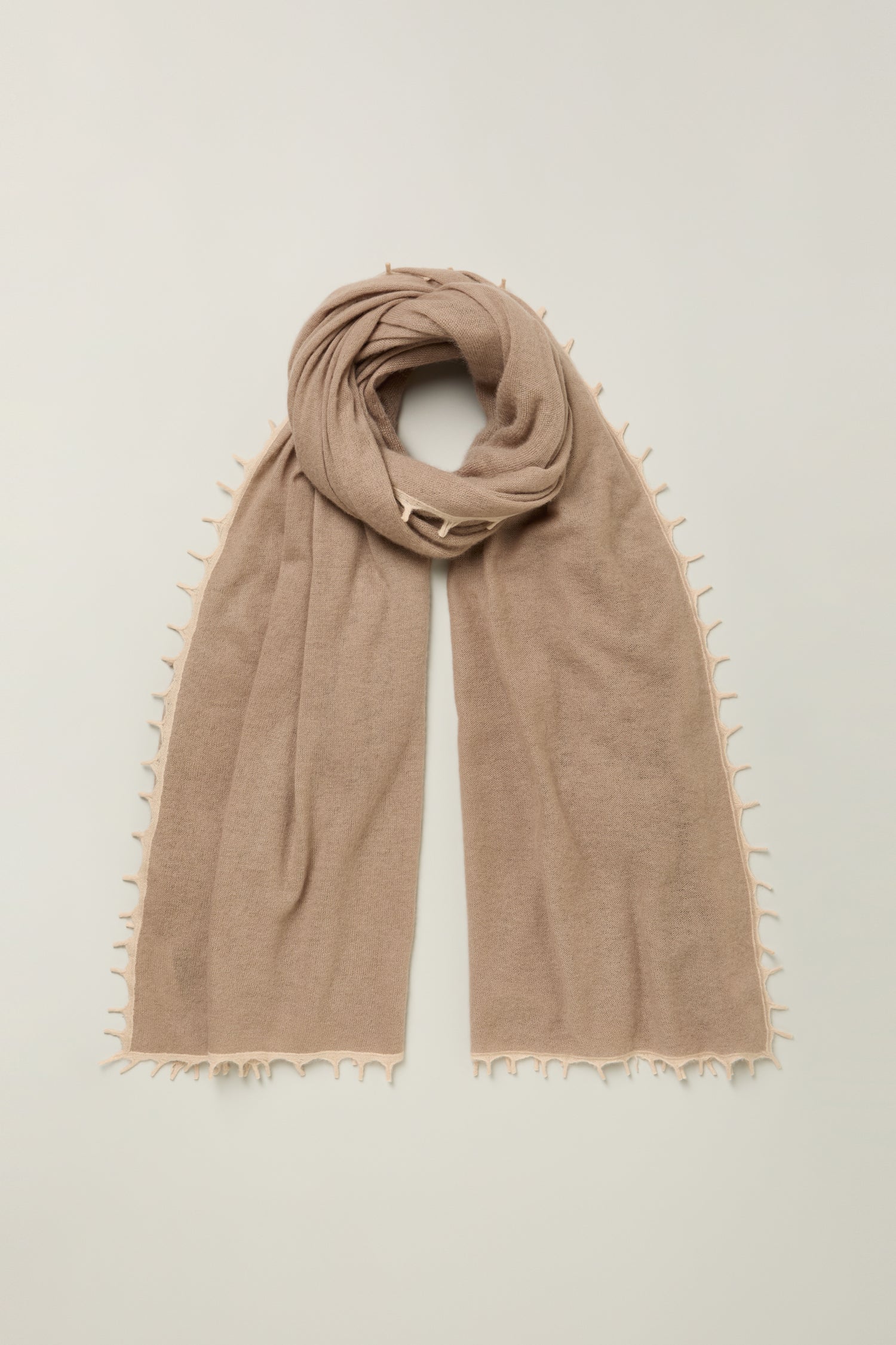 Cream cashmere scarf with contrast trim, crafted for a luxurious feel, and featuring delicate fringed edges laid flat on a neutral background.