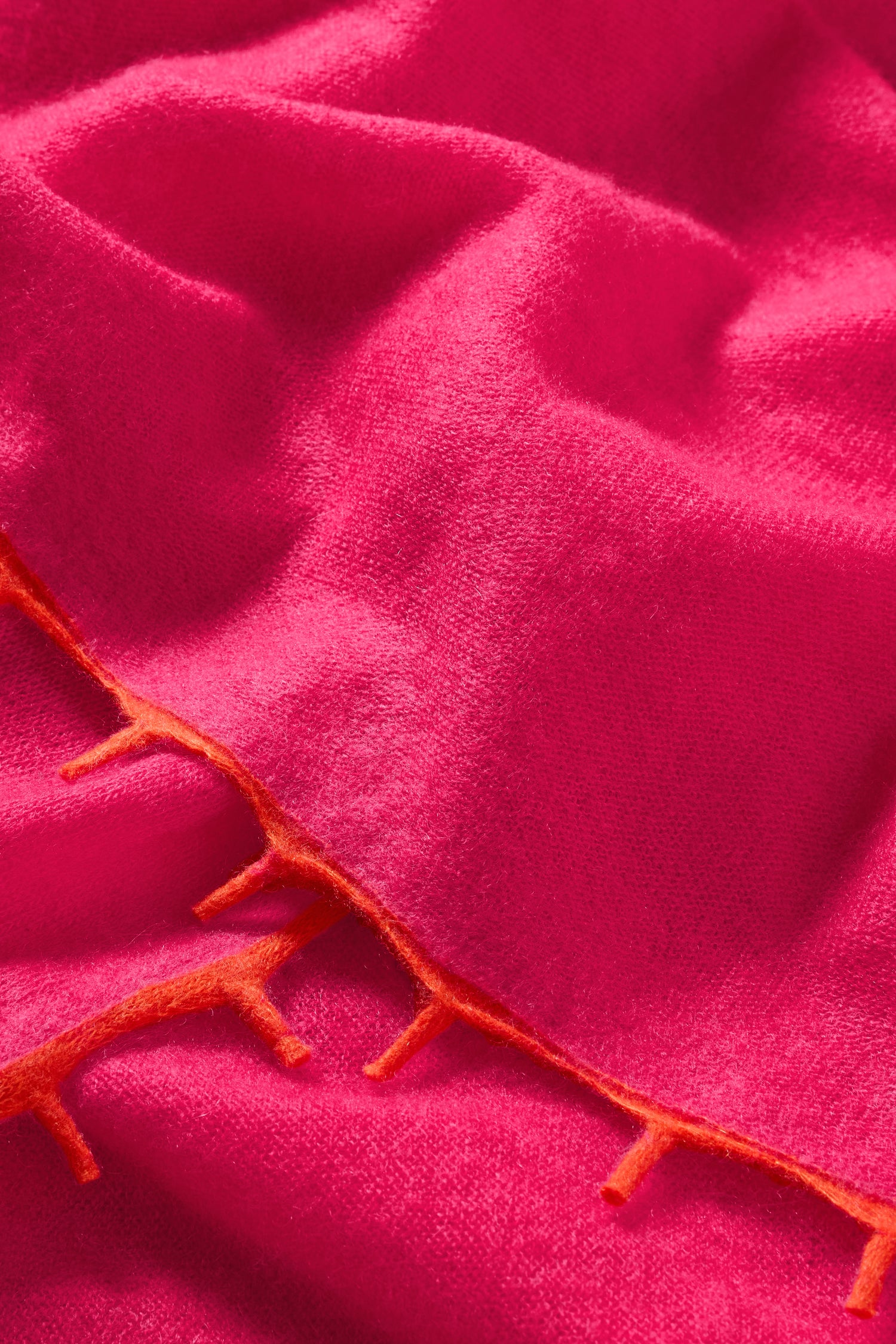 The Contrast Trim Pink Cashmere Scarf features a bright pink hue with orange edges and a soft, slightly textured surface—making it a standout luxury accessory.