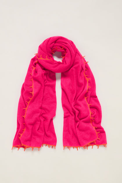 The Contrast Trim Pink Cashmere Scarf features a bright pink hue with orange contrast edging, shown laid flat on a light background.