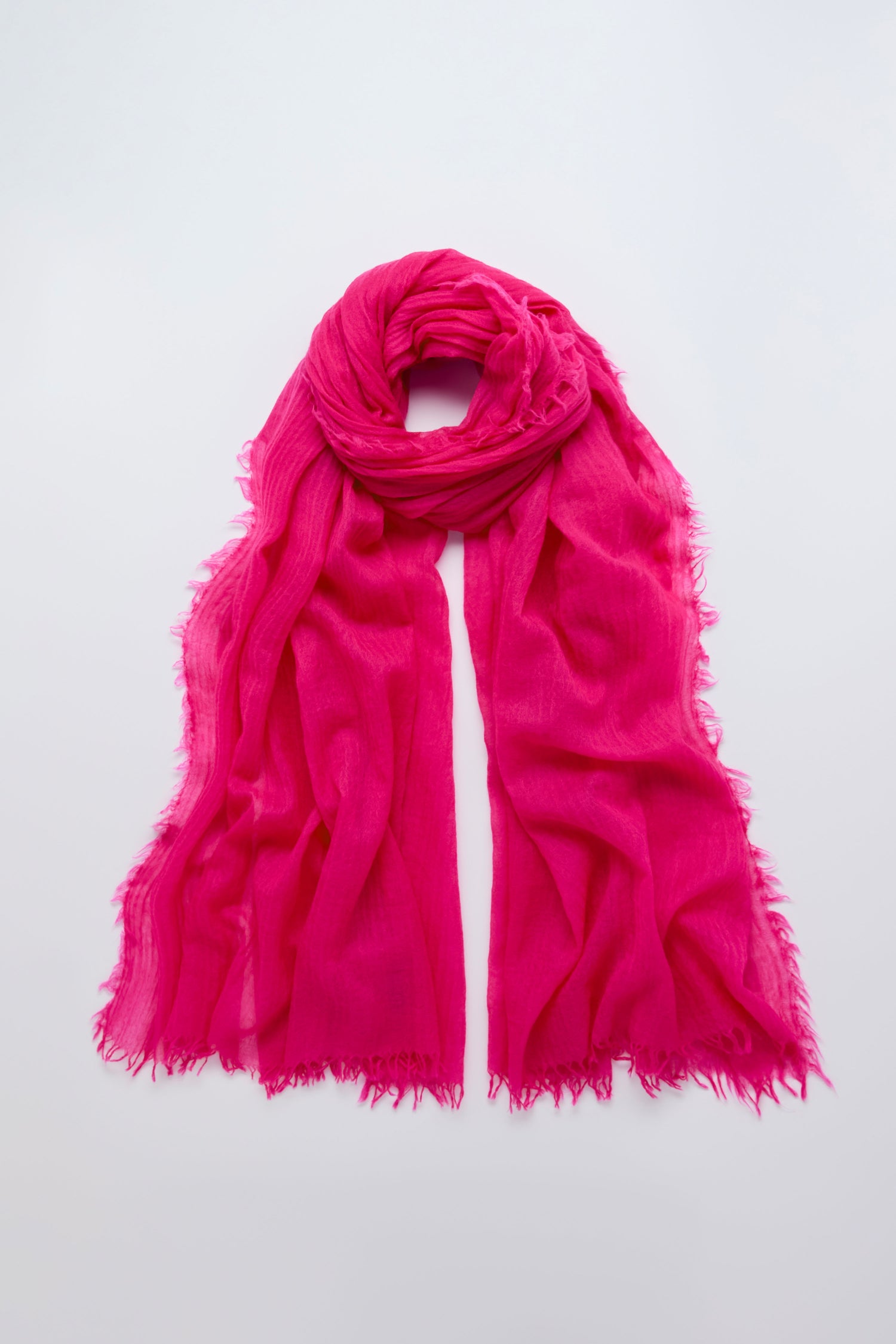 The Hibiscus Fine Wool Fringe Scarf, a fuchsia lightweight accessory with frayed edges, is displayed flat on a plain white background.