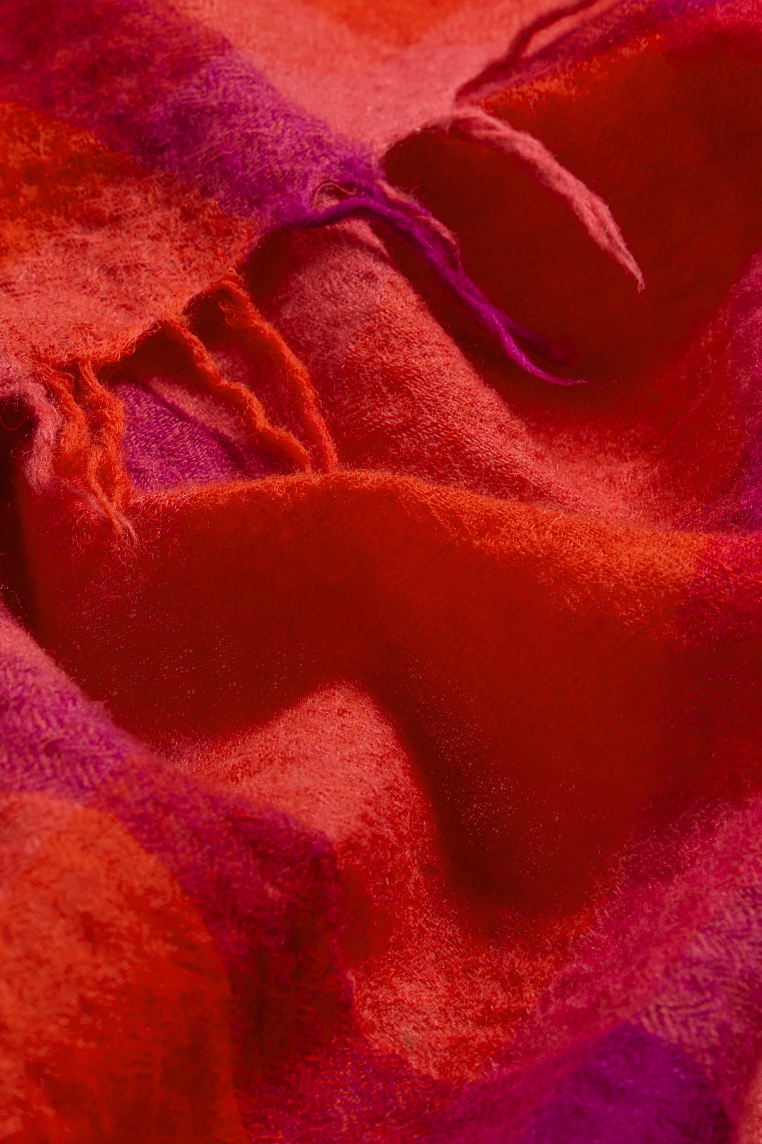 Close-up of the Sunset Check Wool Scarf, featuring soft, fuzzy wool in rich red and purple jewel tones with visible texture and loose threads.