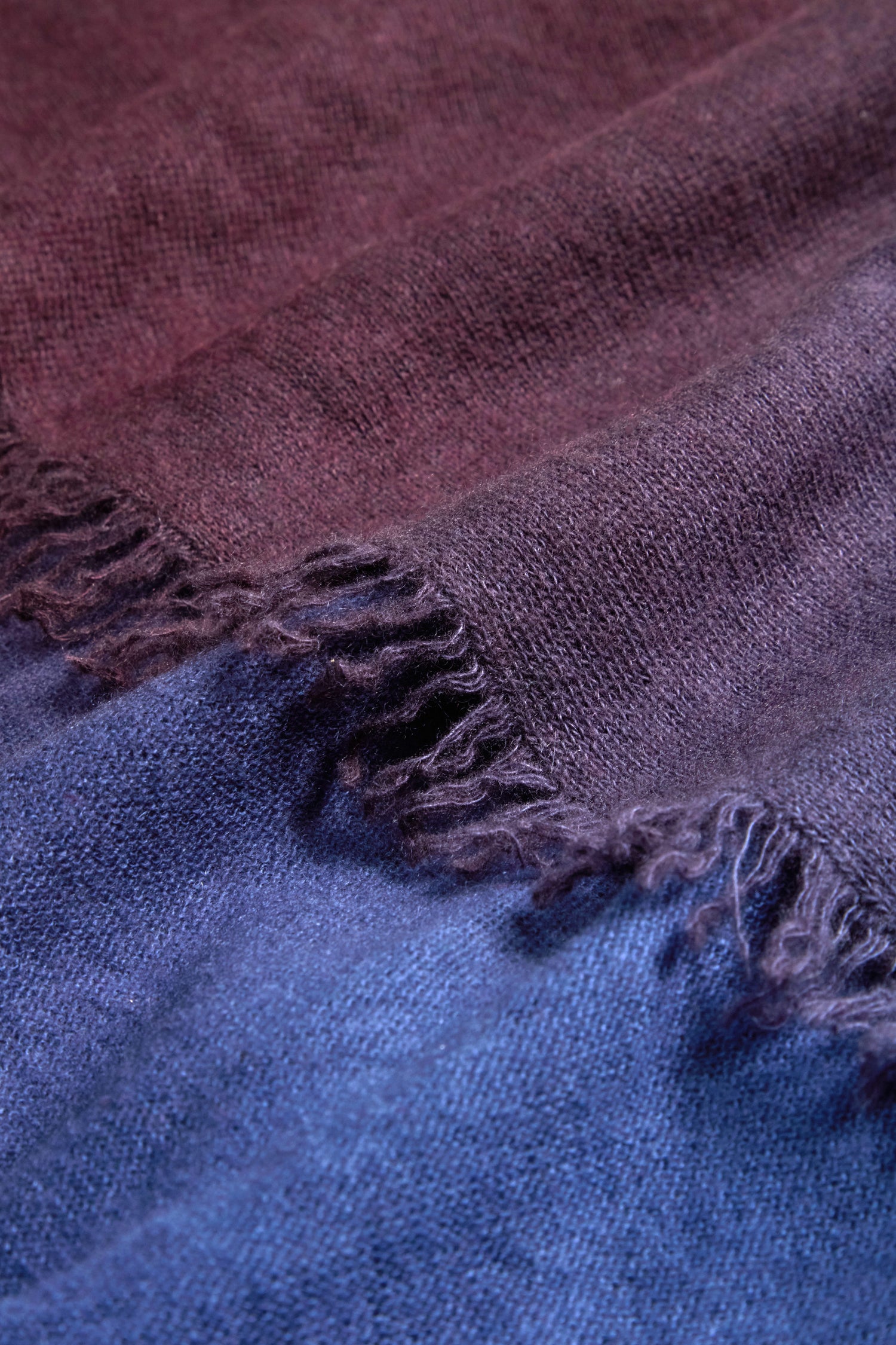 Close-up of the Ombre Cashmere Square Scarf, showcasing frayed edges and a luxe gradient that transitions from maroon at the top to purple in the center and blue at the bottom.