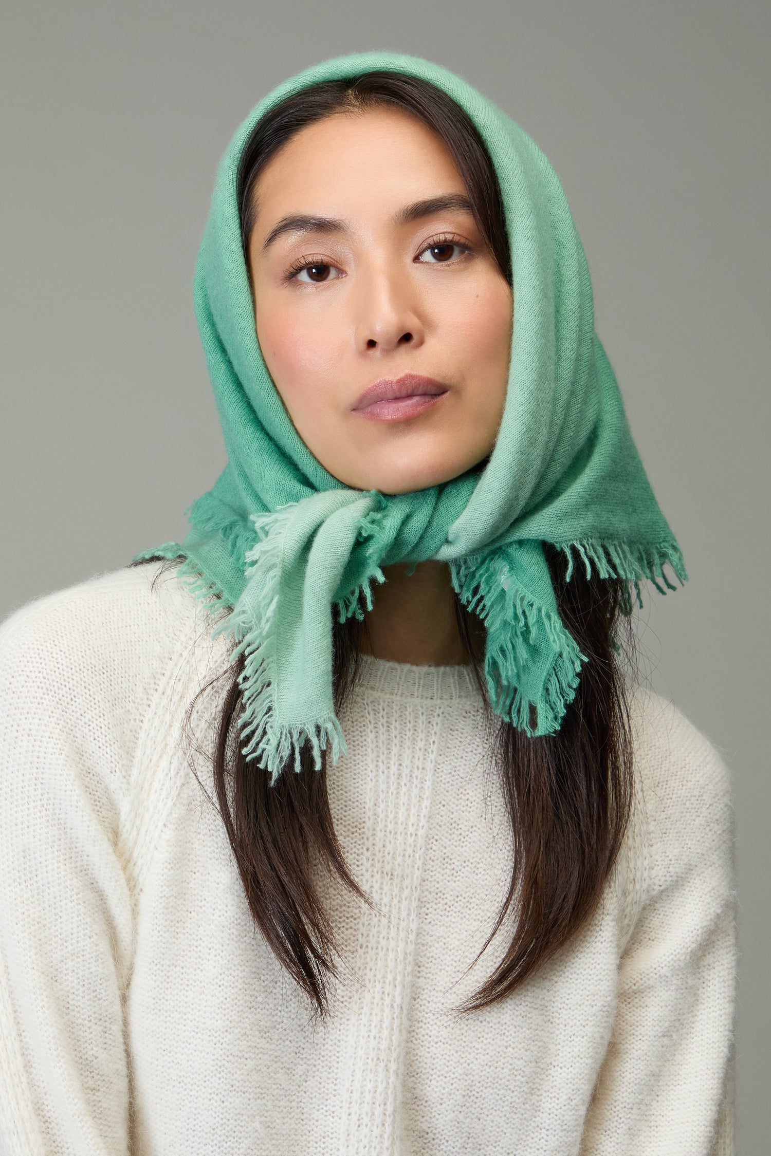 A person in a cream sweater wears the Ombre Cashmere Square Scarf wrapped over their head, looking directly at the camera against a neutral background.