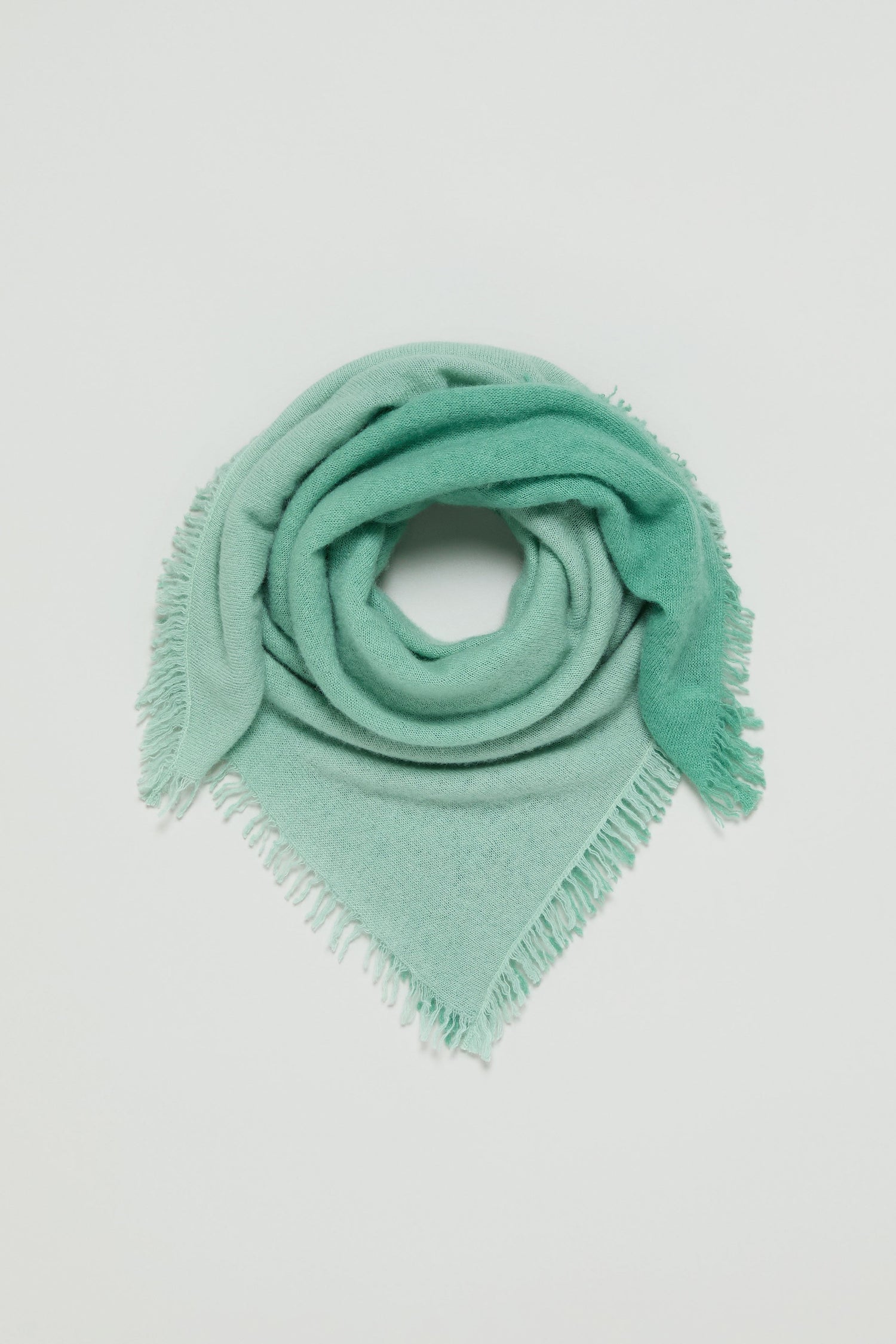 The Ombre Cashmere Square Scarf in light green is folded into a triangle and coiled neatly on a plain white background.